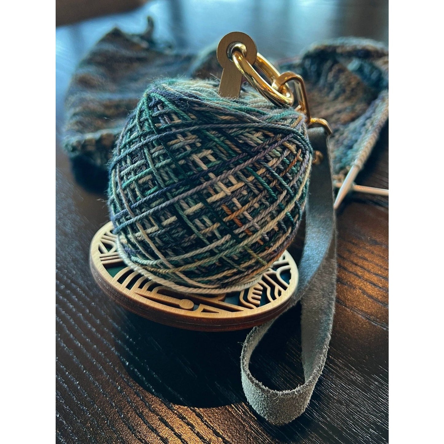 lemonwood art deco stitch marker with green variegated yarn cake on wooden base with leather strap and knitting