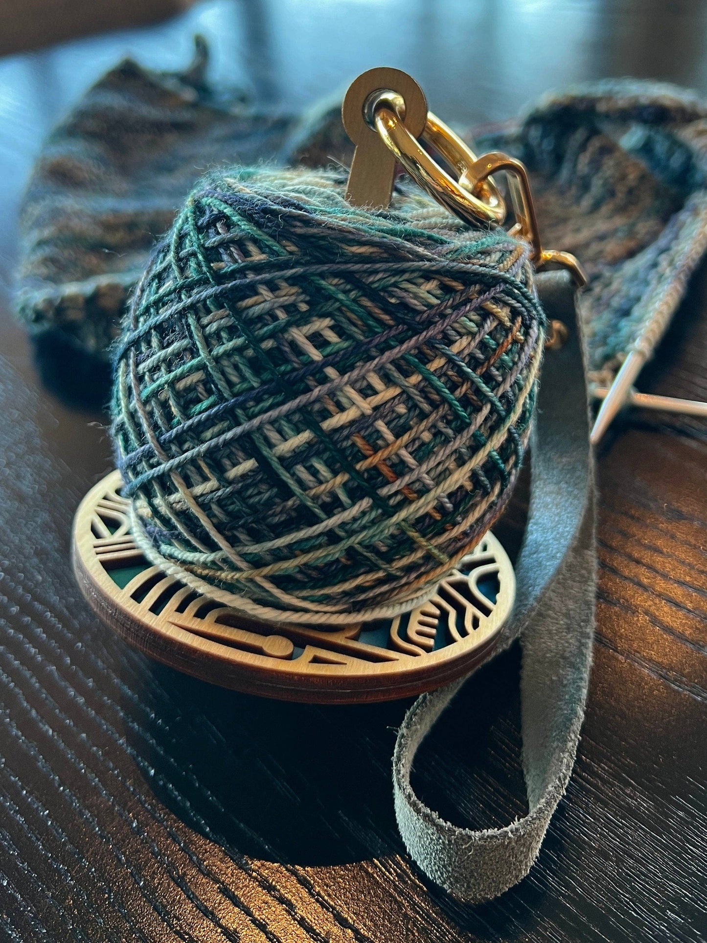 lemonwood art deco stitch marker with green variegated yarn cake on wooden base with leather strap and knitting