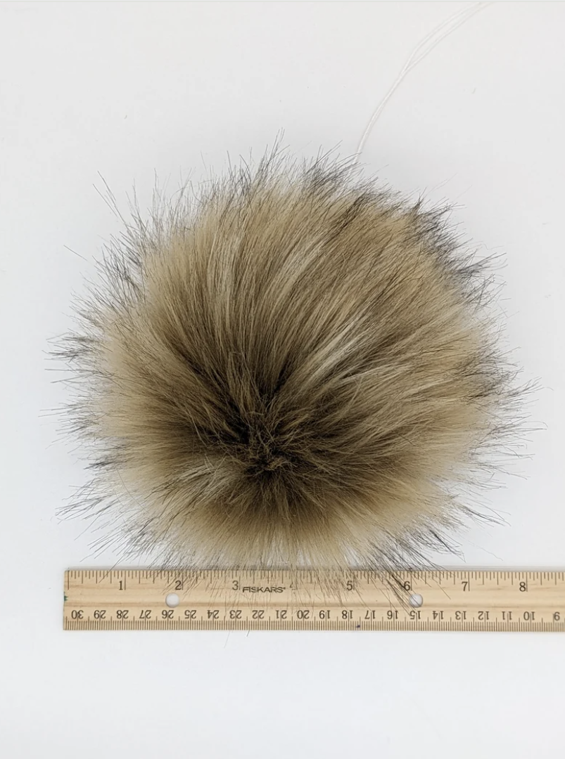 Blonde faux fur pom pom accessory on a measuring ruler for size reference