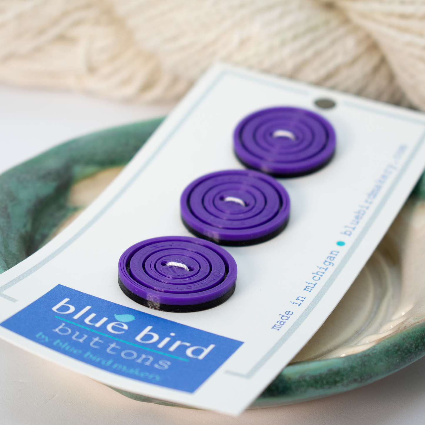 Set of three purple blue bird makery buttons displayed on a ceramic dish for crafting projects