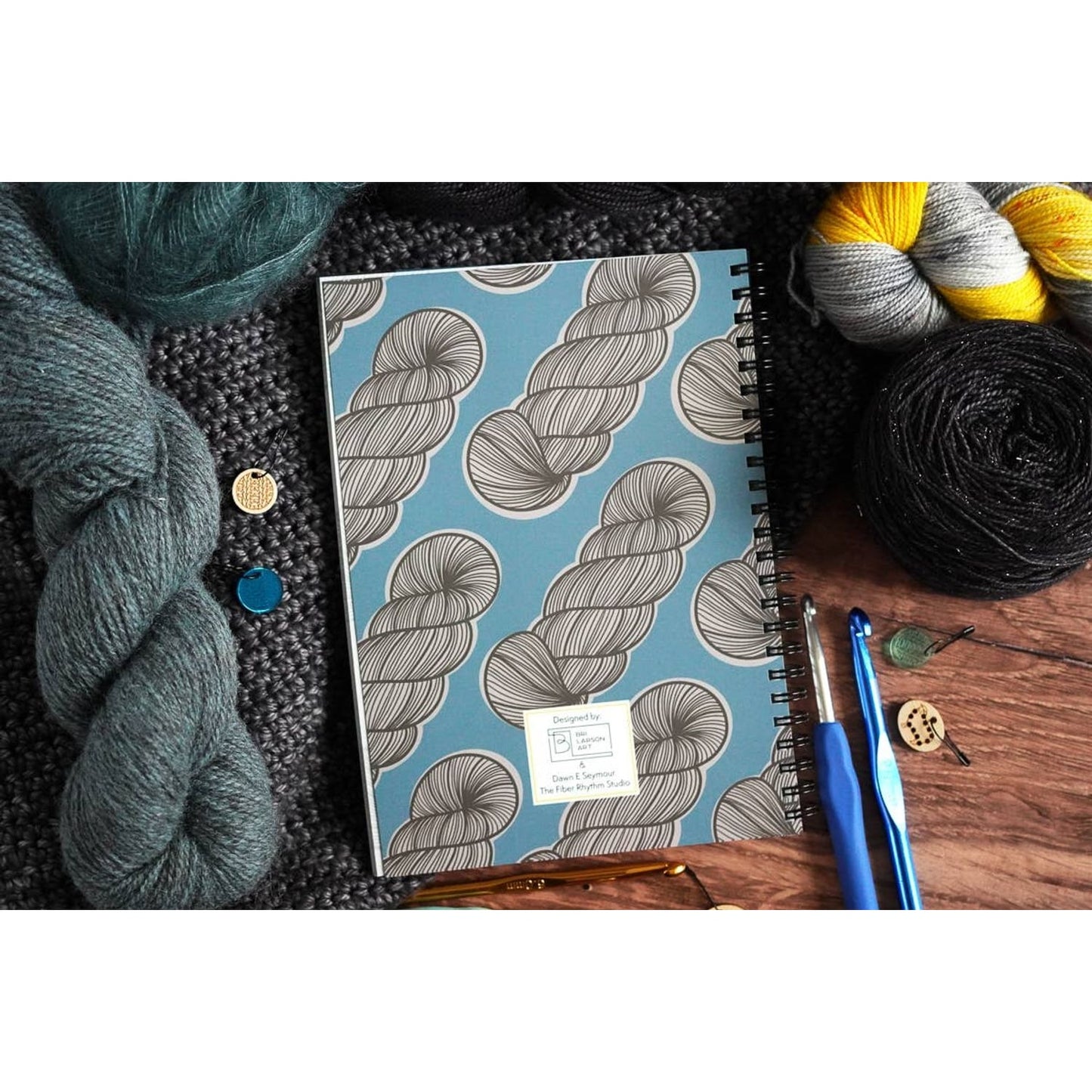crochet pattern organizer notebook spiral bound with blue skein print cover surrounded by yarn hooks and buttons