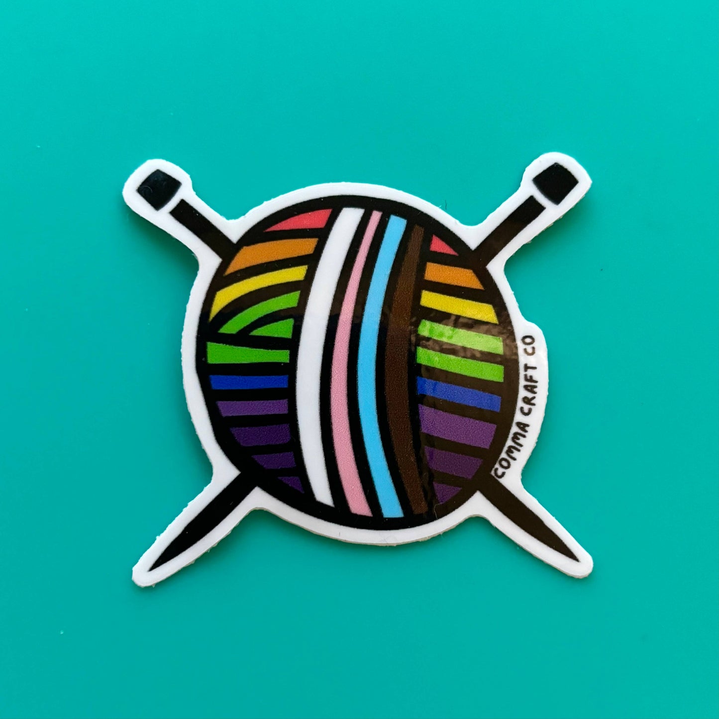 Comma Craft Co intersectional pride knitting sticker featuring colorful yarn ball with knitting needles