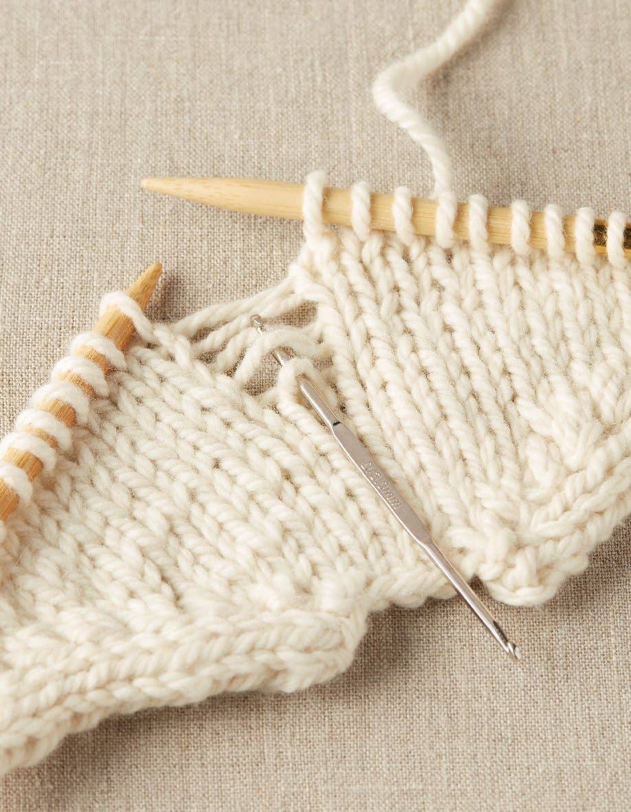 Cocoknits stitch fixer tool used on cream-colored knitting with wooden needles on beige fabric