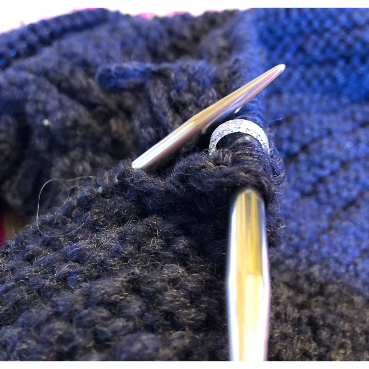 Close-up of stitch markers for crocheting attached to knitting needles and yarn in progress