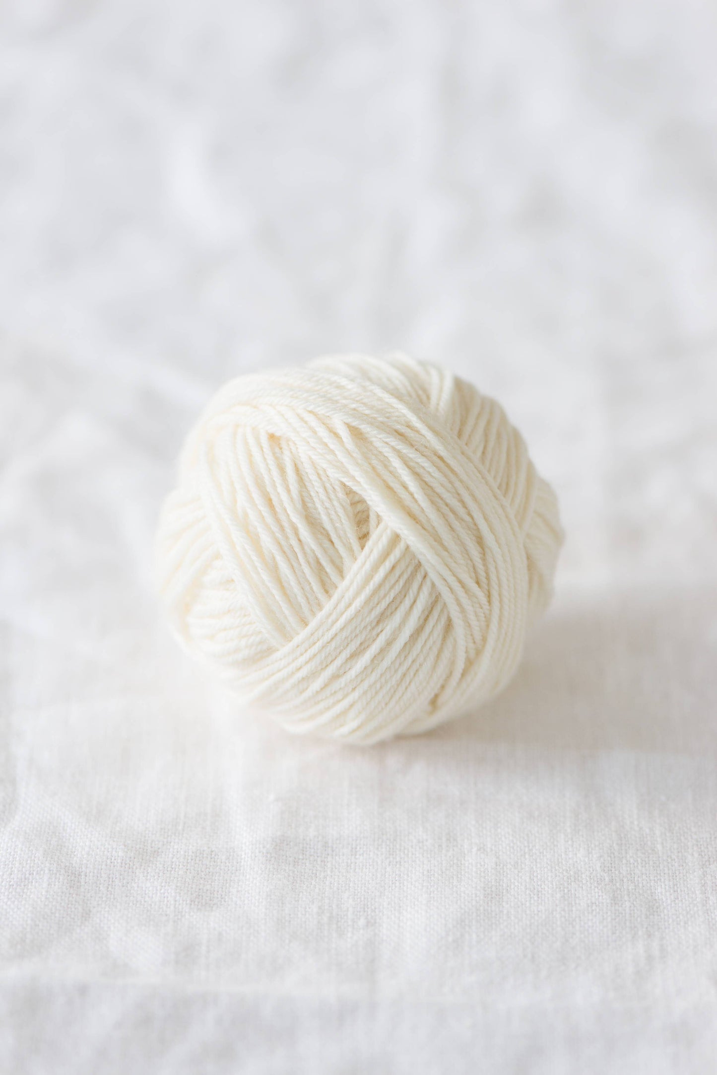 Quince & Co. superwash merino fingering yarn ball in natural white color on white fabric background