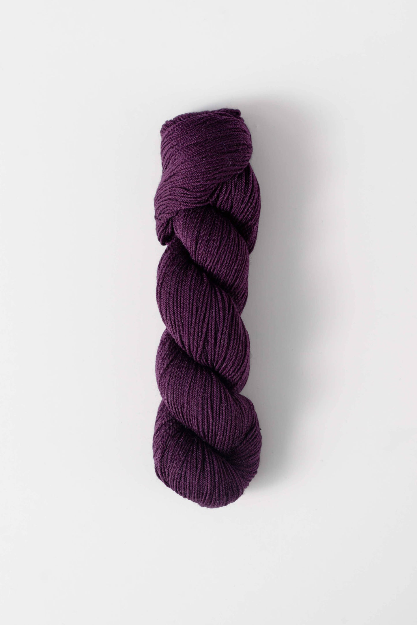 Quince and Co superwash merino fingering yarn in deep purple color skein on white background