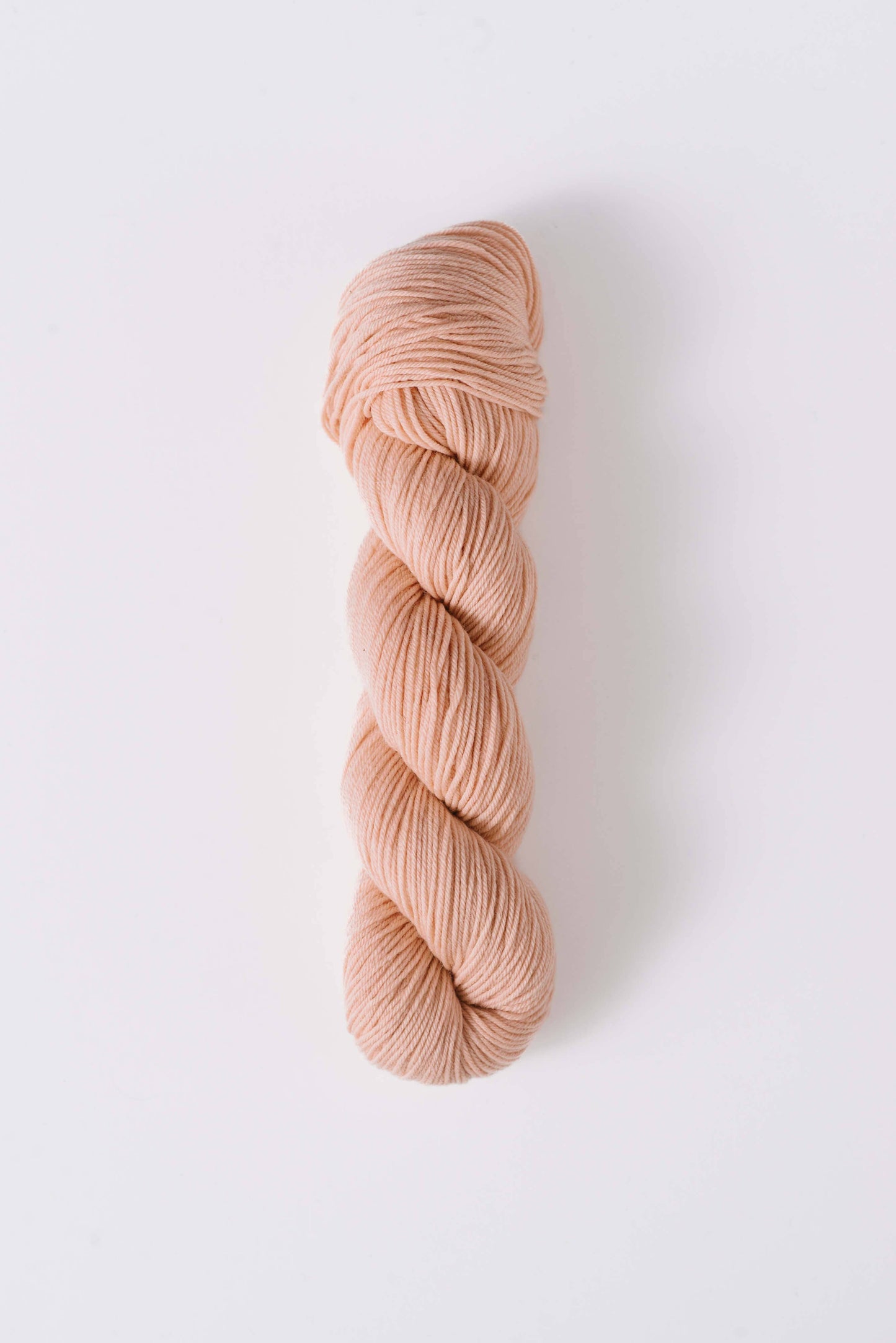 Quince & Co. soft peach colored superwash merino fingering yarn skein isolated on white background