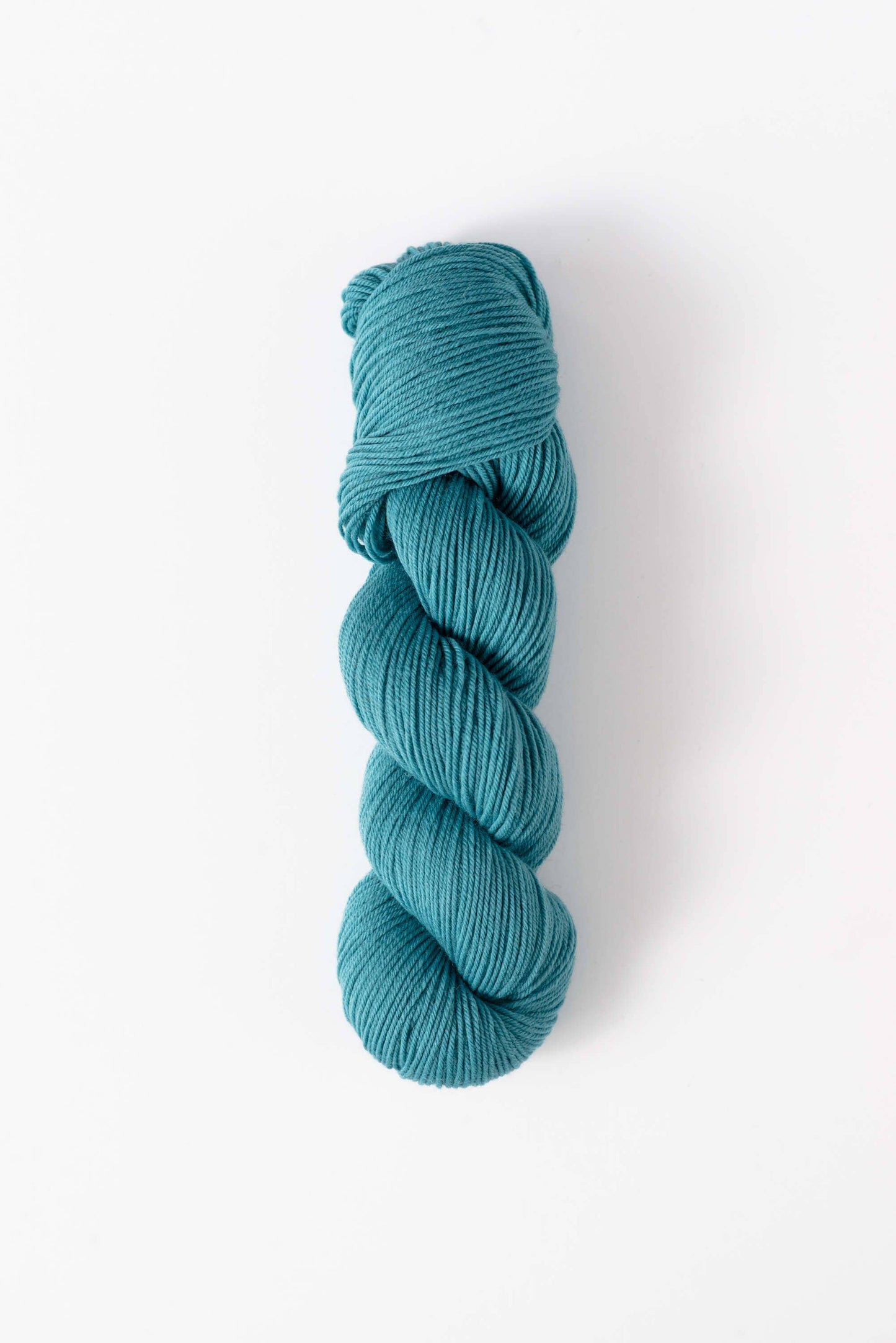 Quince & Co. superwash merino fingering yarn in teal blue skein on white background