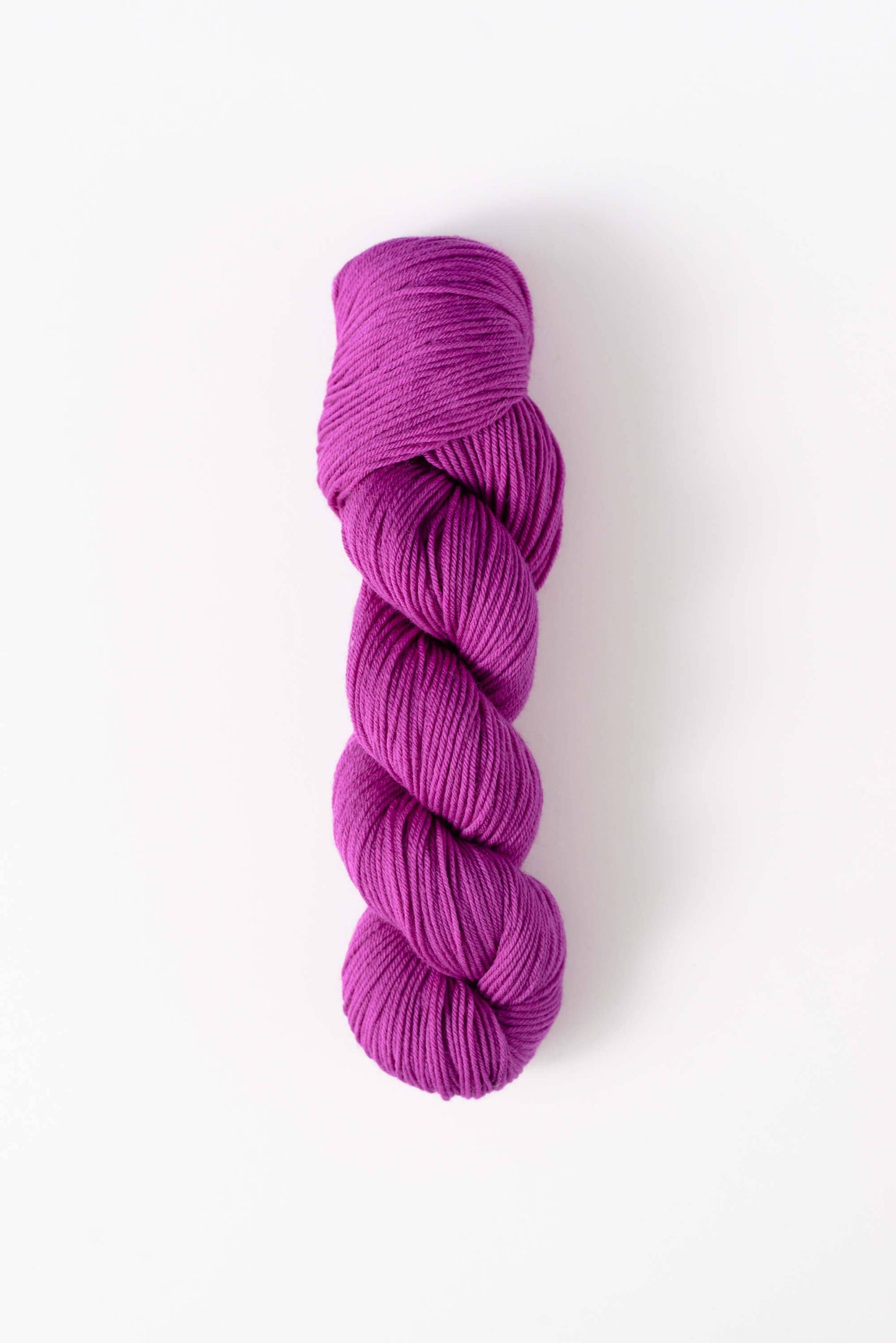 Quince and Co superwash merino fingering yarn in vibrant purple skein on white background