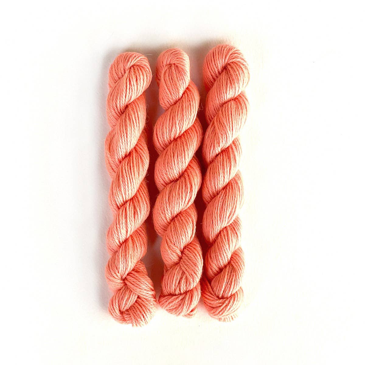 Three skeins of Kelbourne Woolens Perennial Minis yarn in coral color for knitting or crochet projects