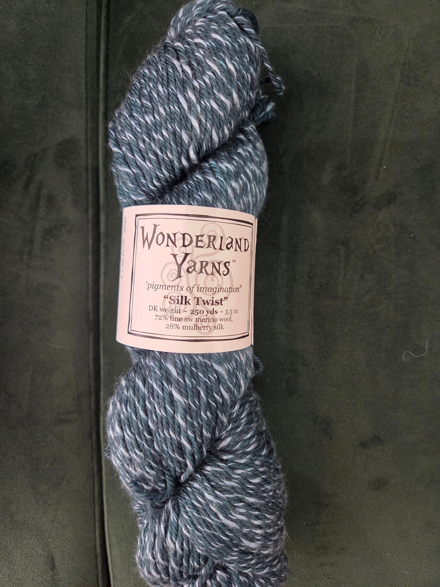 Wonderland Yarns Silk Twist blue gray marled DK weight skein with white flecks on dark fabric