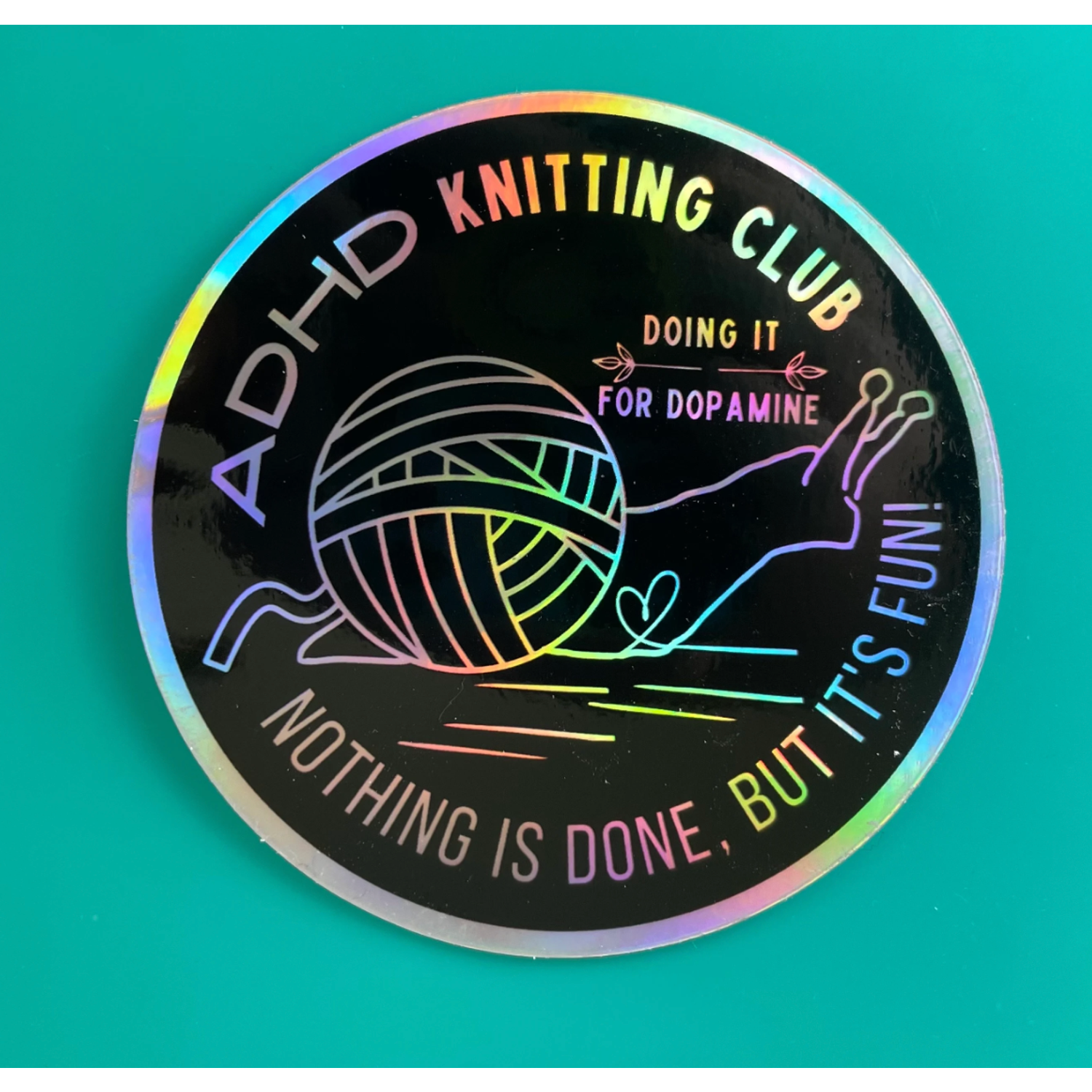 Holographic round sticker featuring yarn and needles with ADHD Knitting Club text and slogan fun knitting stickers for craft…