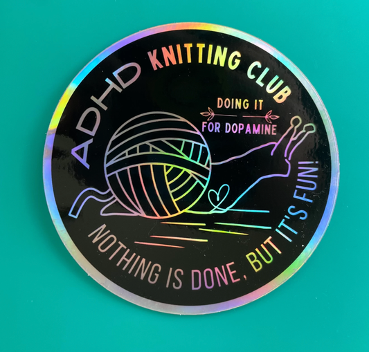 Holographic round sticker featuring yarn and needles with ADHD Knitting Club text and slogan fun knitting stickers for crafters