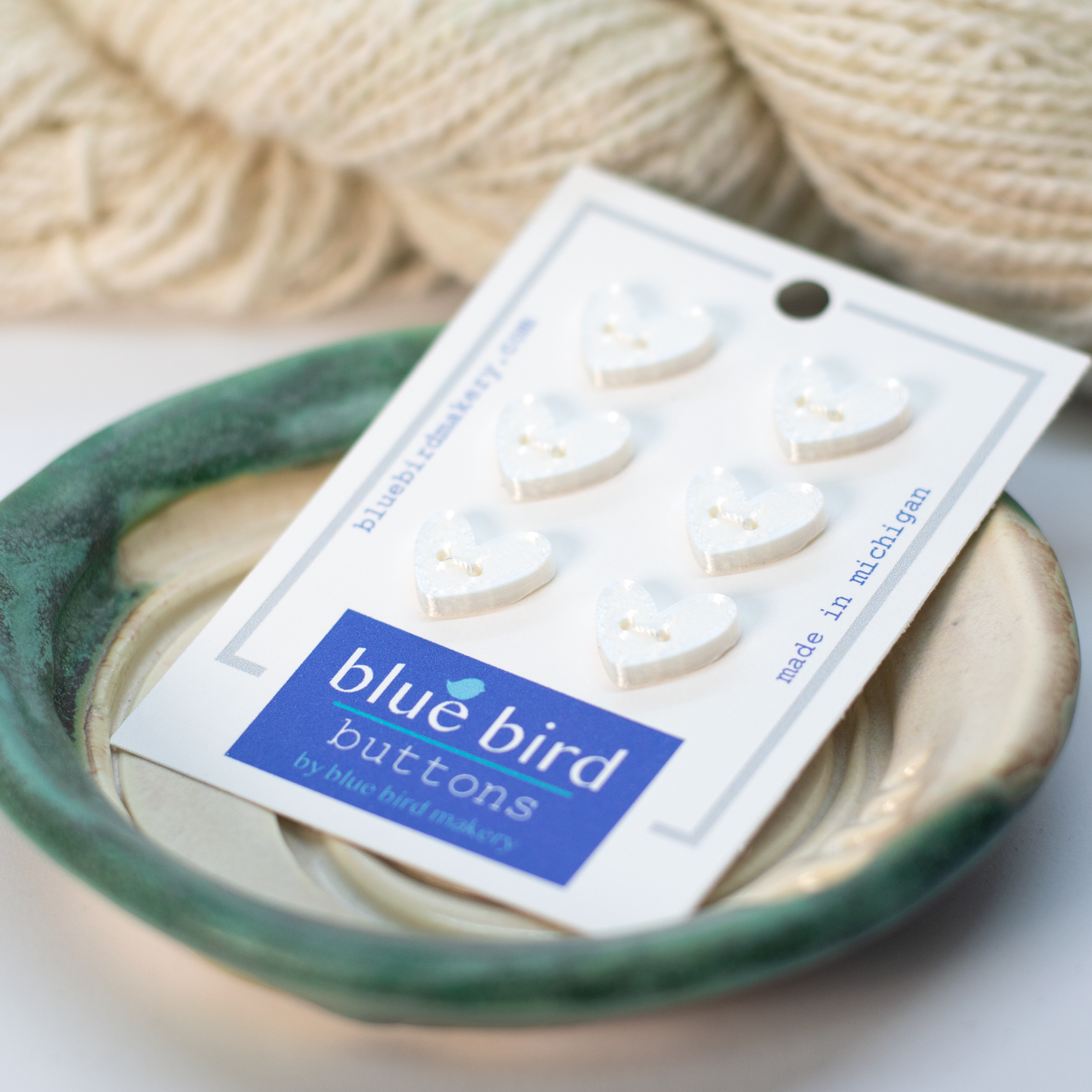 Pack of white heart-shaped pink 12mm craft buttons from Blue Bird Makery on a decorative plate