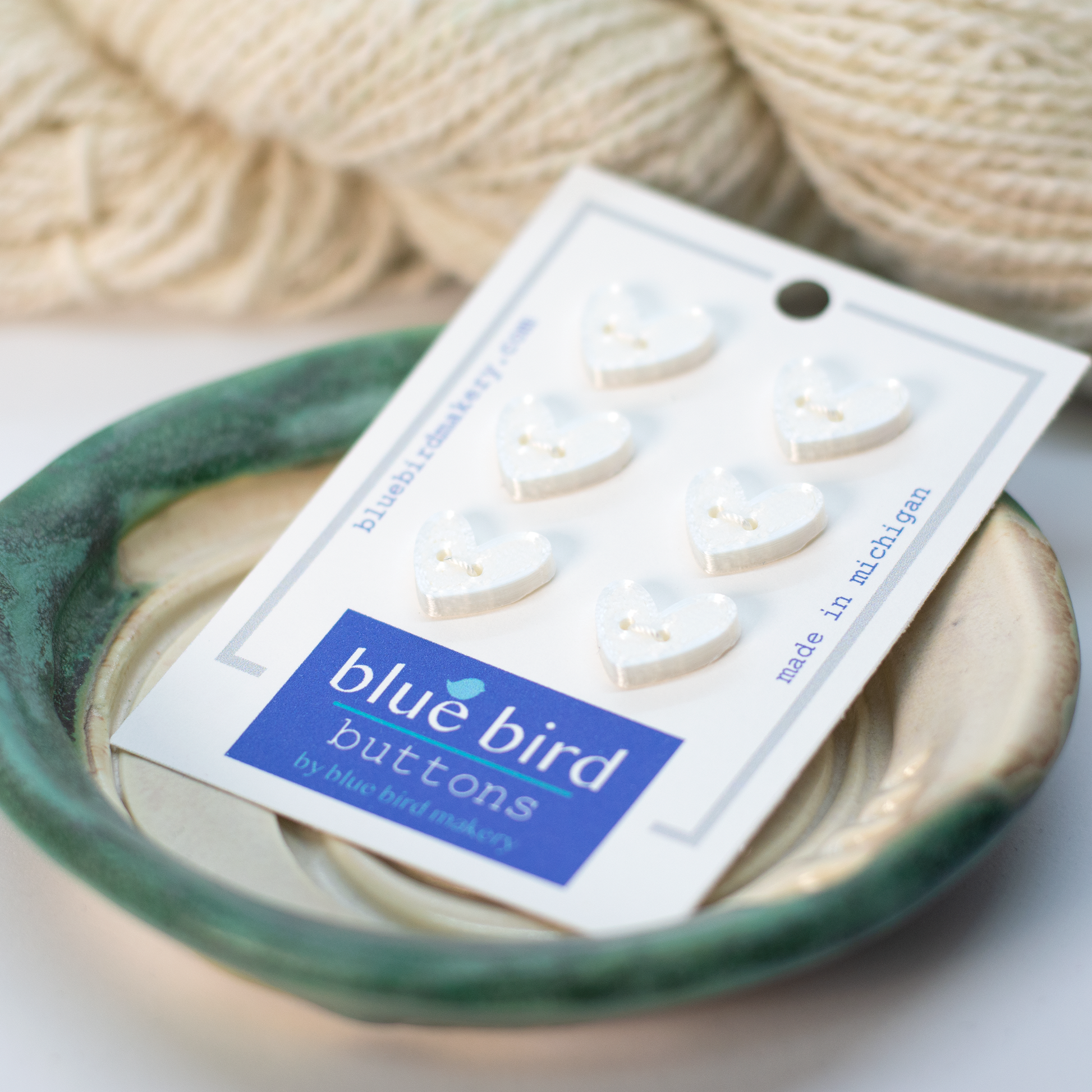 Pack of white heart-shaped pink 12mm craft buttons from Blue Bird Makery on a decorative plate