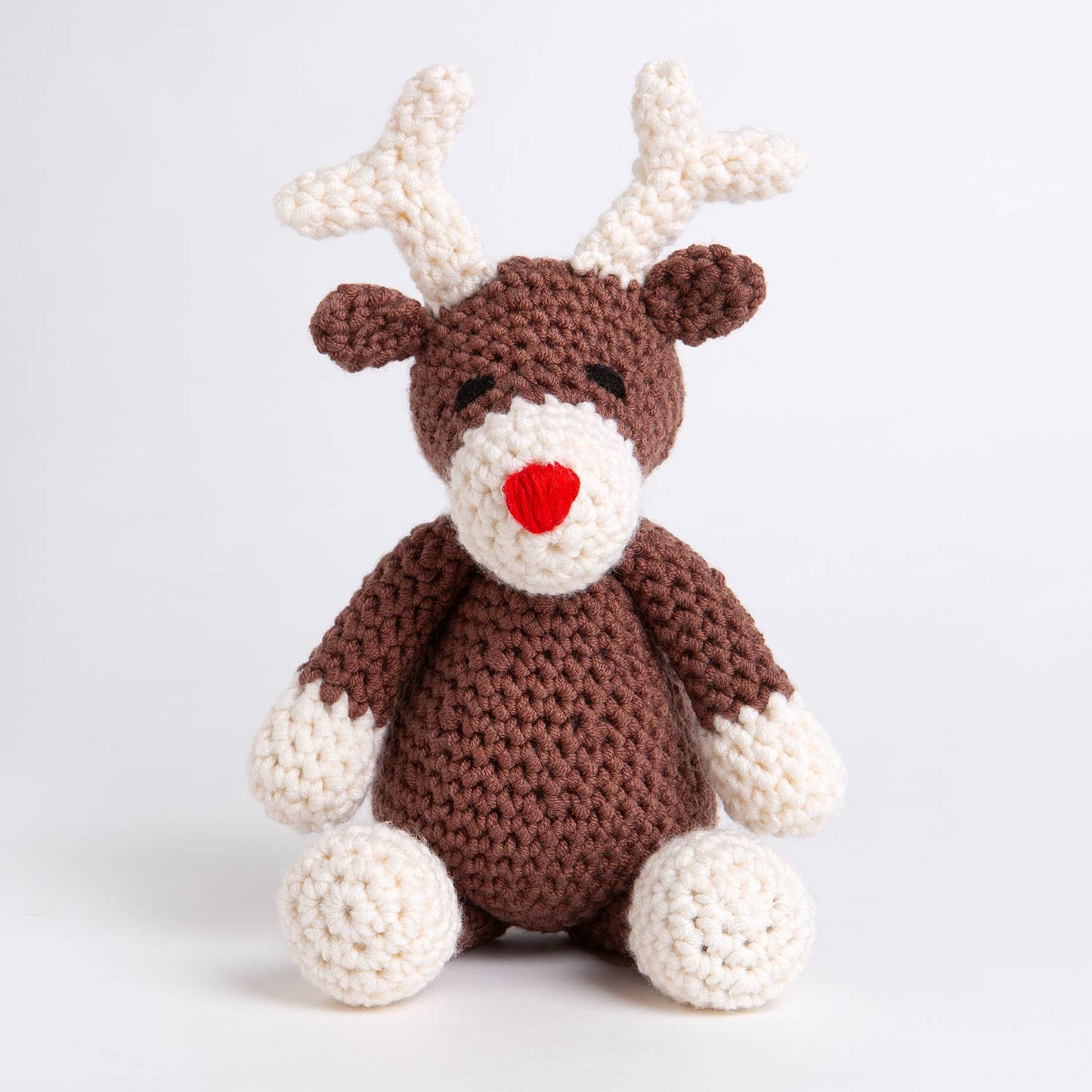 Belle the Reindeer crochet pattern by Wool Couture Company showing a brown crochet reindeer with white antlers and red nose