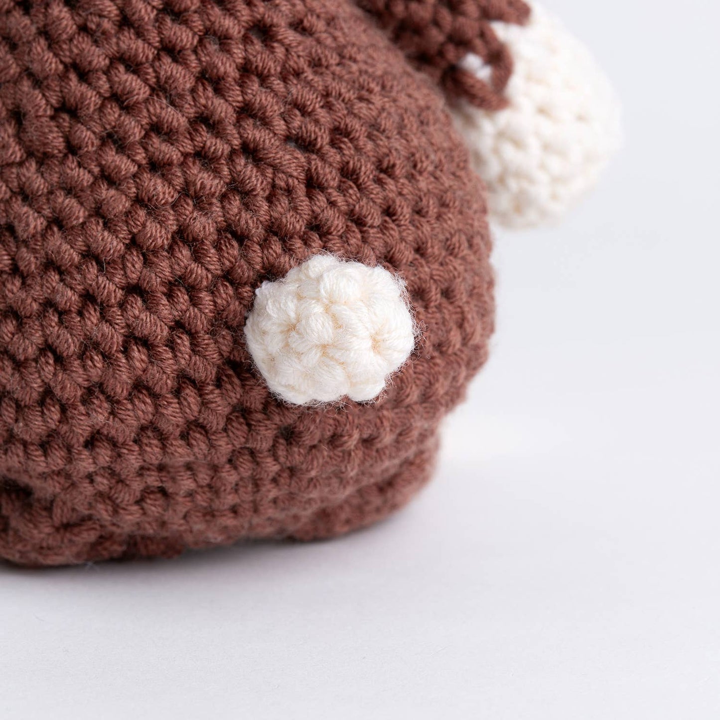 Close up of brown amigurumi reindeer with white pompom tail showcasing Belle the Reindeer crochet pattern