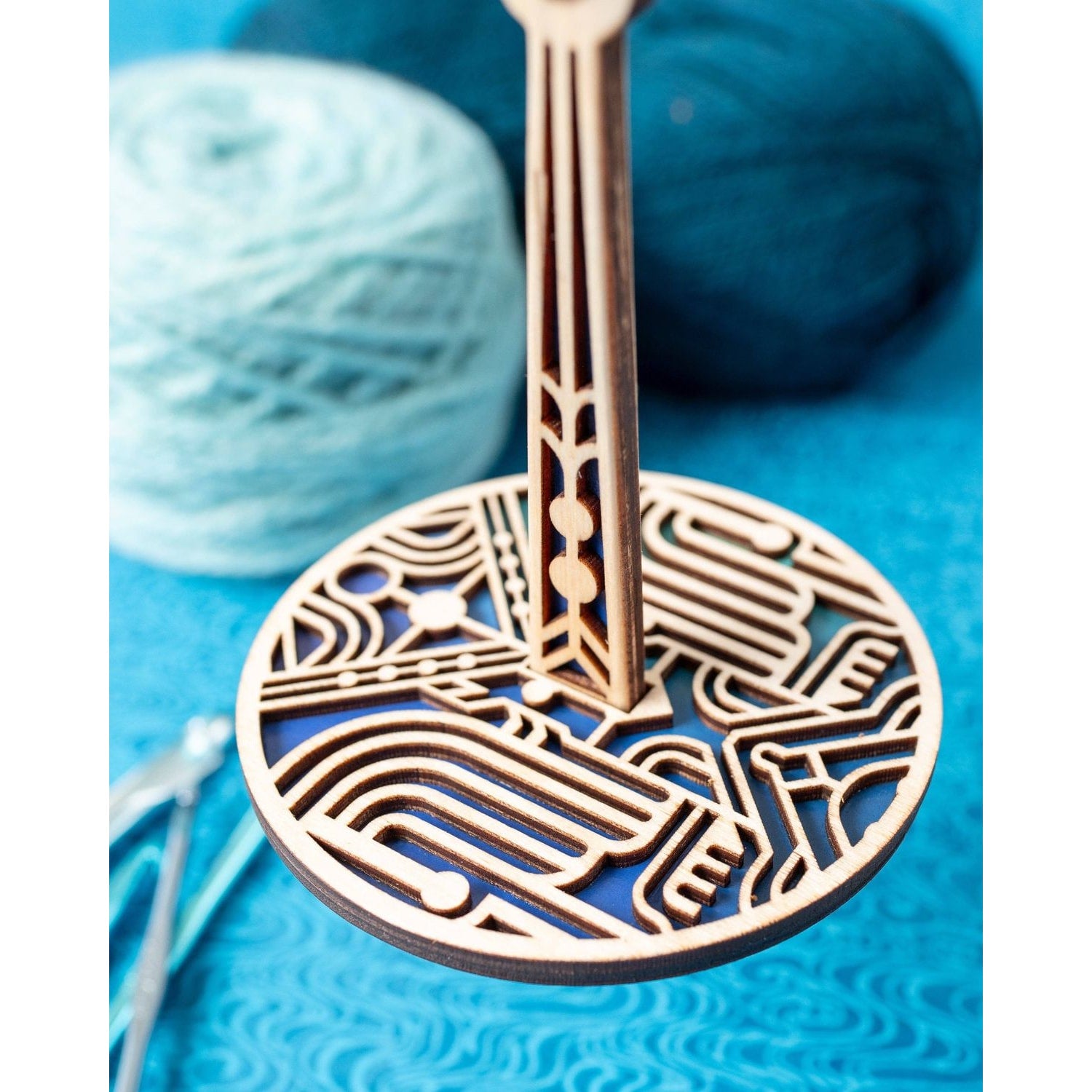 lemonwood art deco stitch marker wooden round geometric holder on stand with intricate cutouts beside blue yarn balls