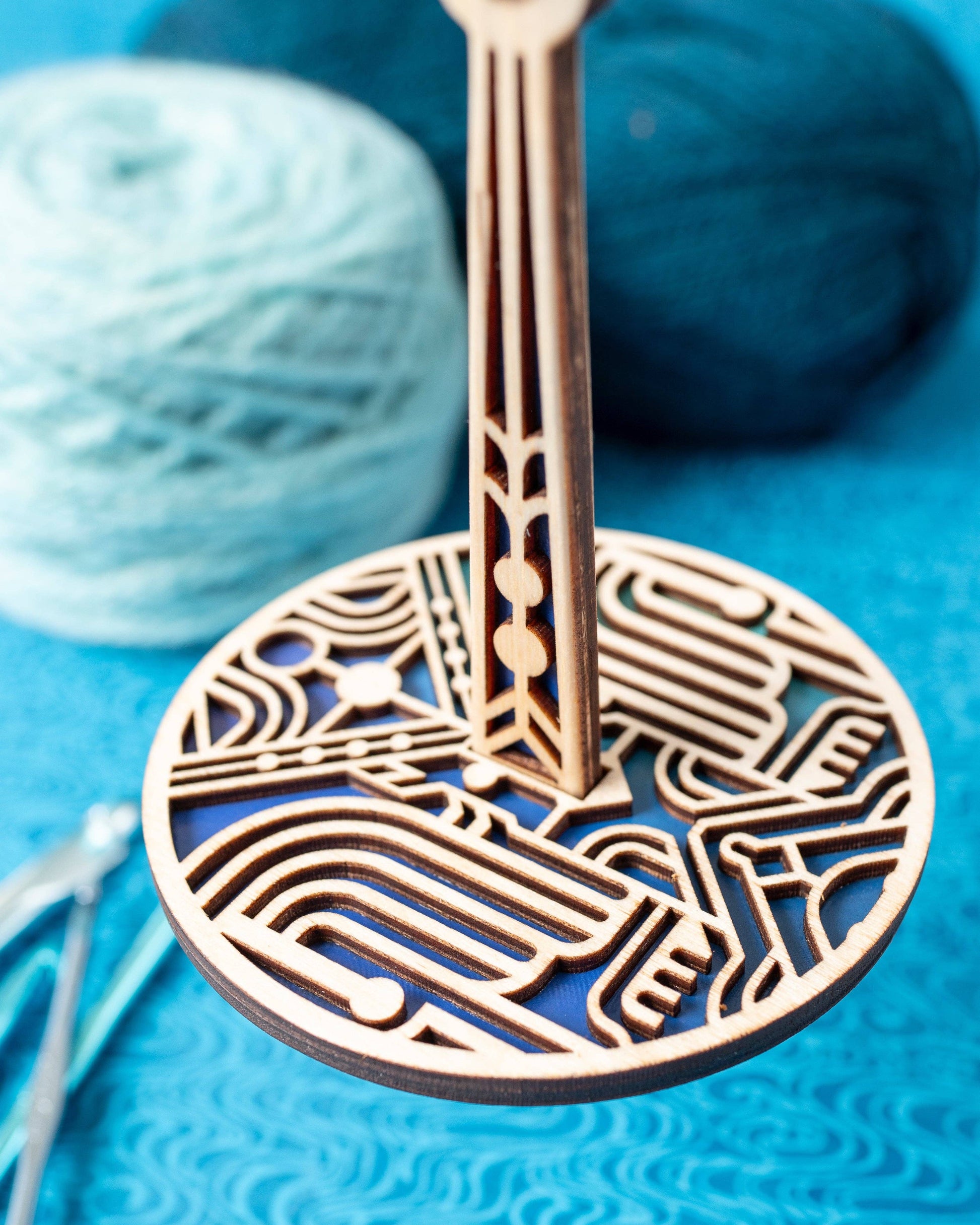 lemonwood art deco stitch marker wooden round geometric holder on stand with intricate cutouts beside blue yarn balls
