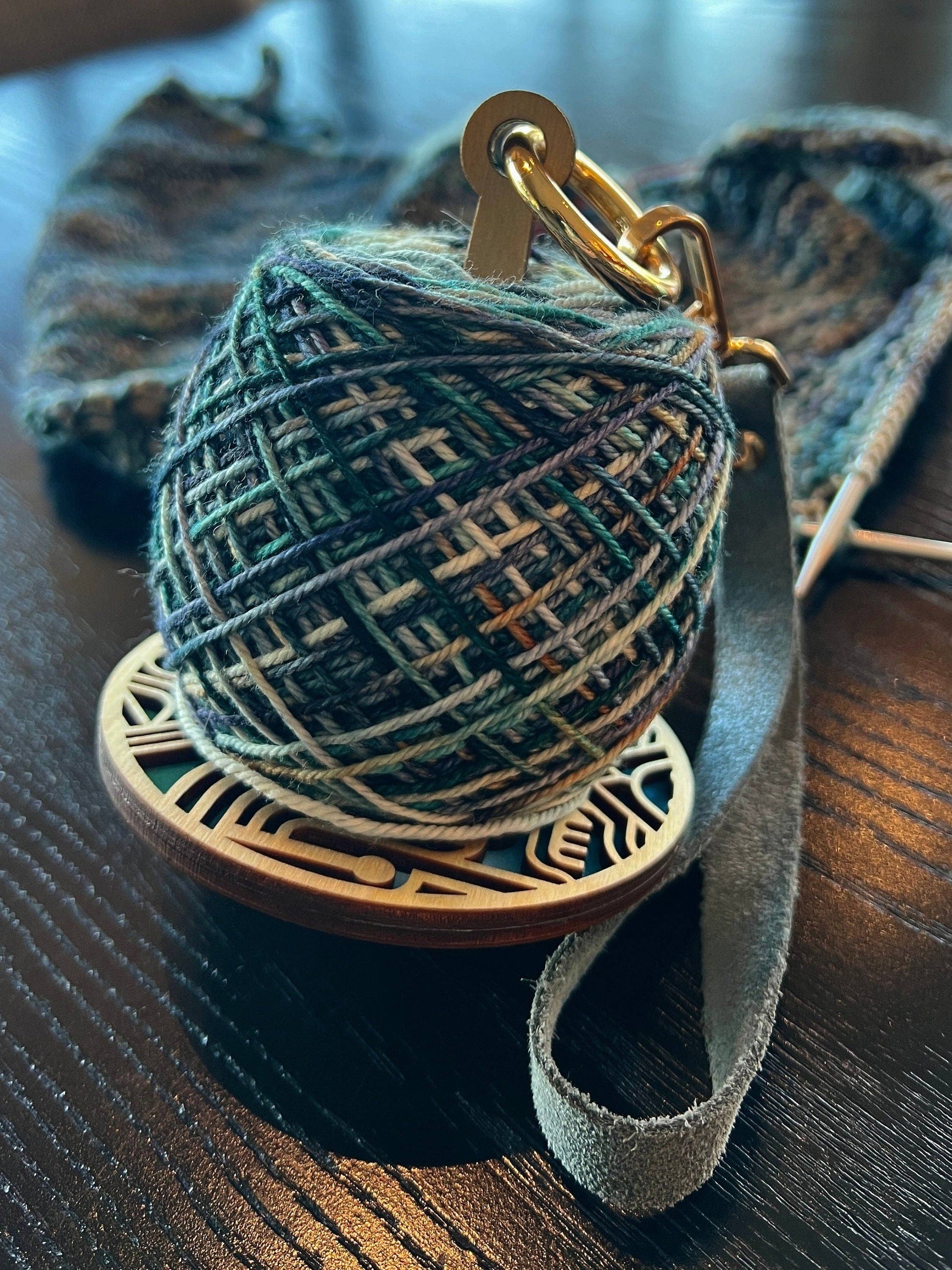lemonwood art deco stitch marker with green variegated yarn cake on wooden base with leather strap and knitting