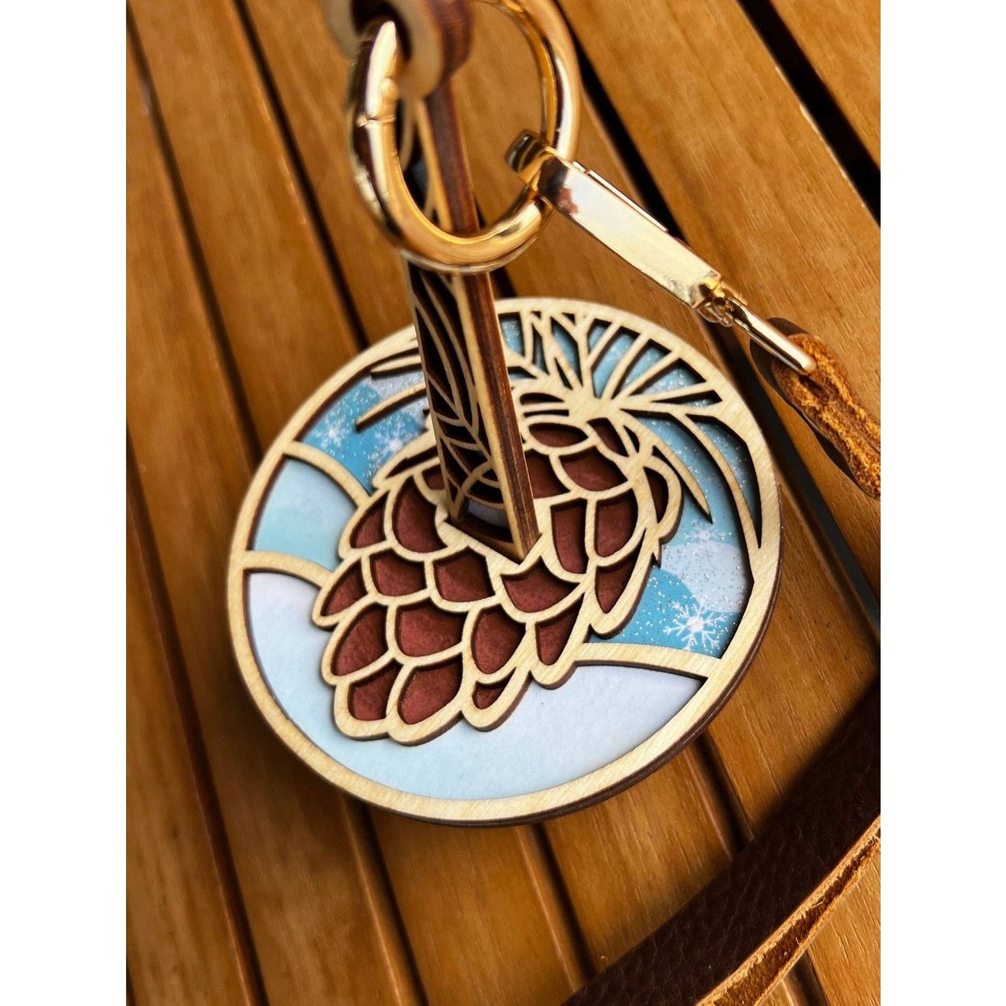 Round wooden keychain with carved wooden pinecone knitting accessory on brass ring and leather strap