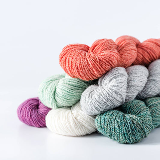 Kelbourne Woolens stacked skeins in coral gray mint purple white and teal for knitting fingering weight 100% wool yarn