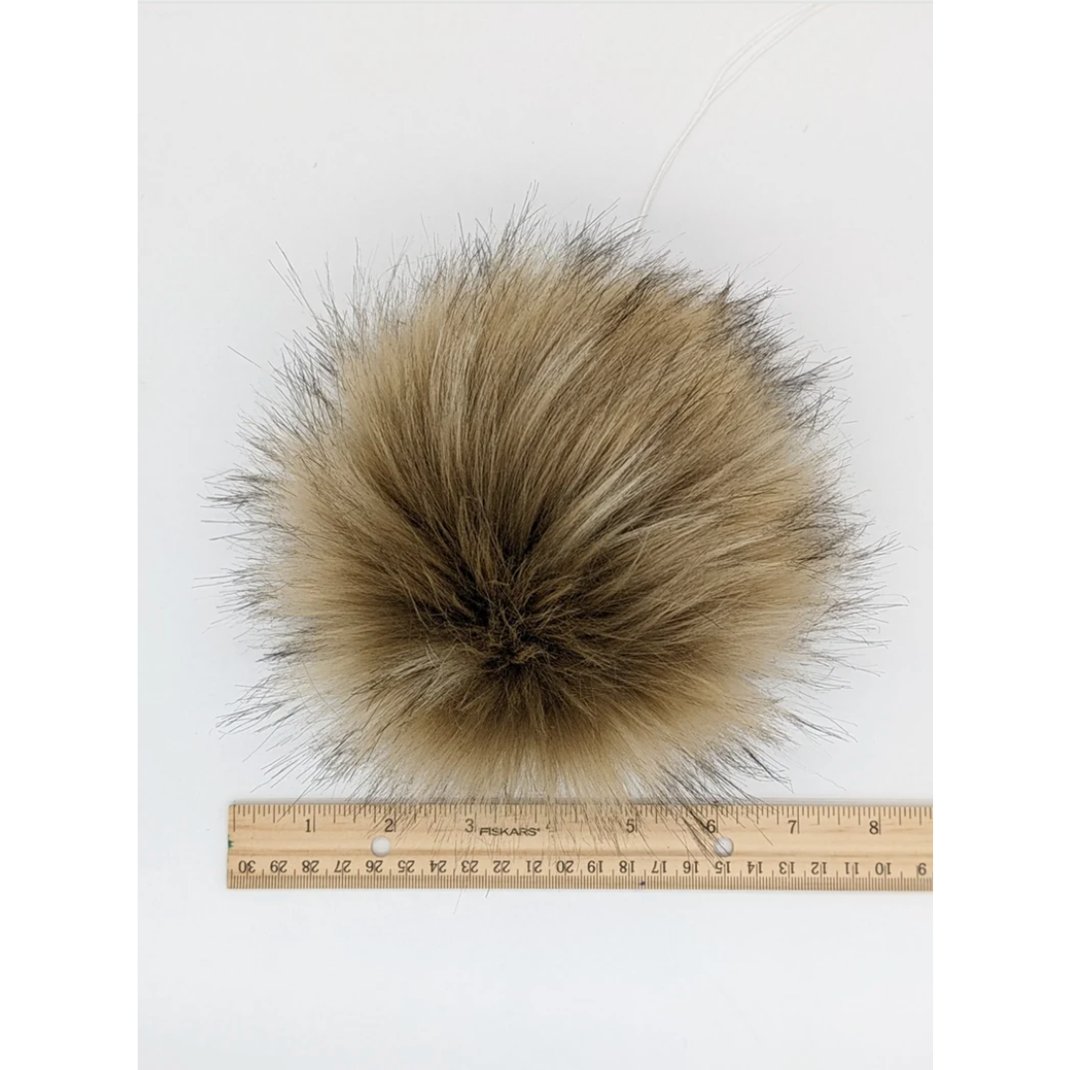 Blonde faux fur pom pom accessory on a measuring ruler for size reference