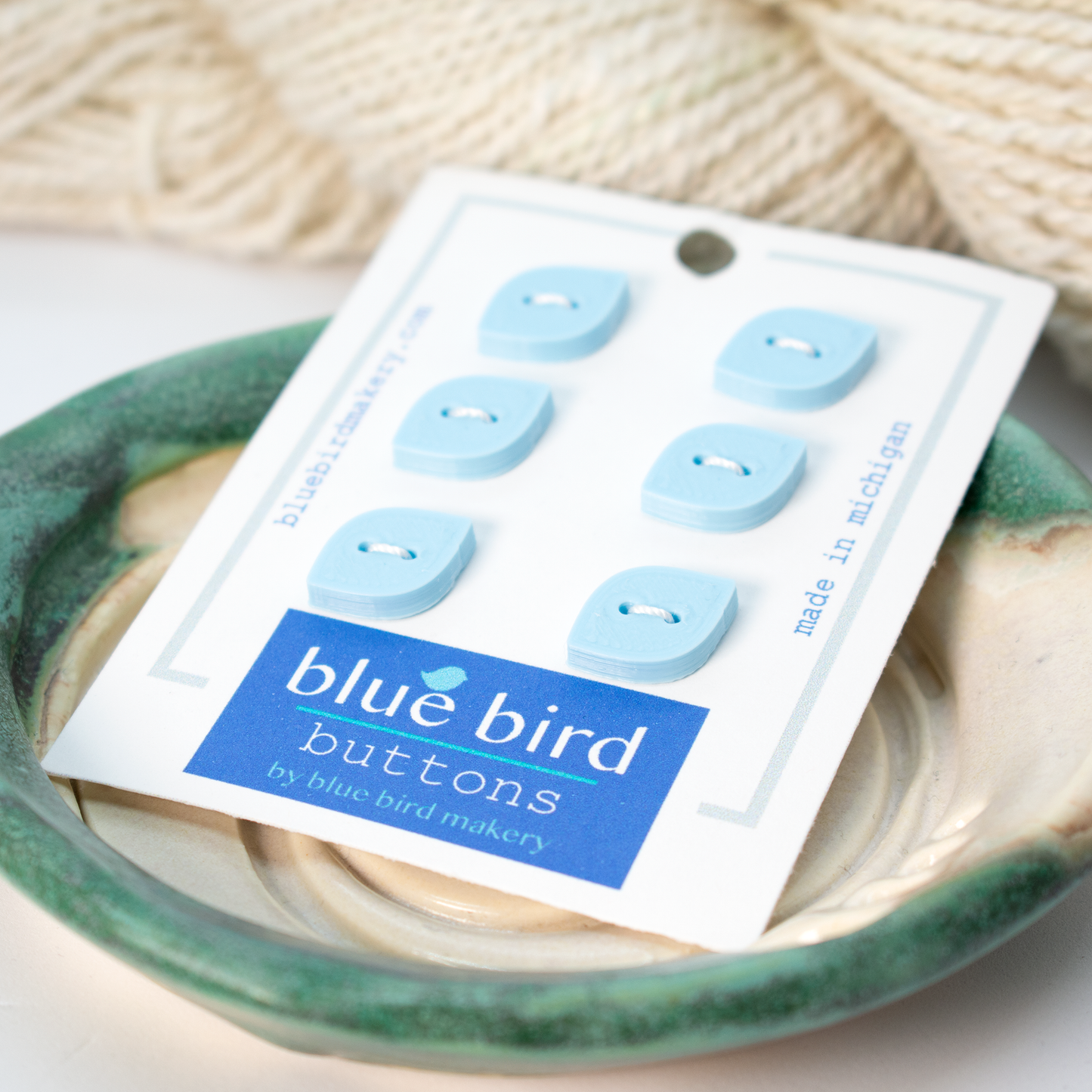 Set of 6 12mm blue bird buttons displayed on a ceramic dish by Blue Bird Makery