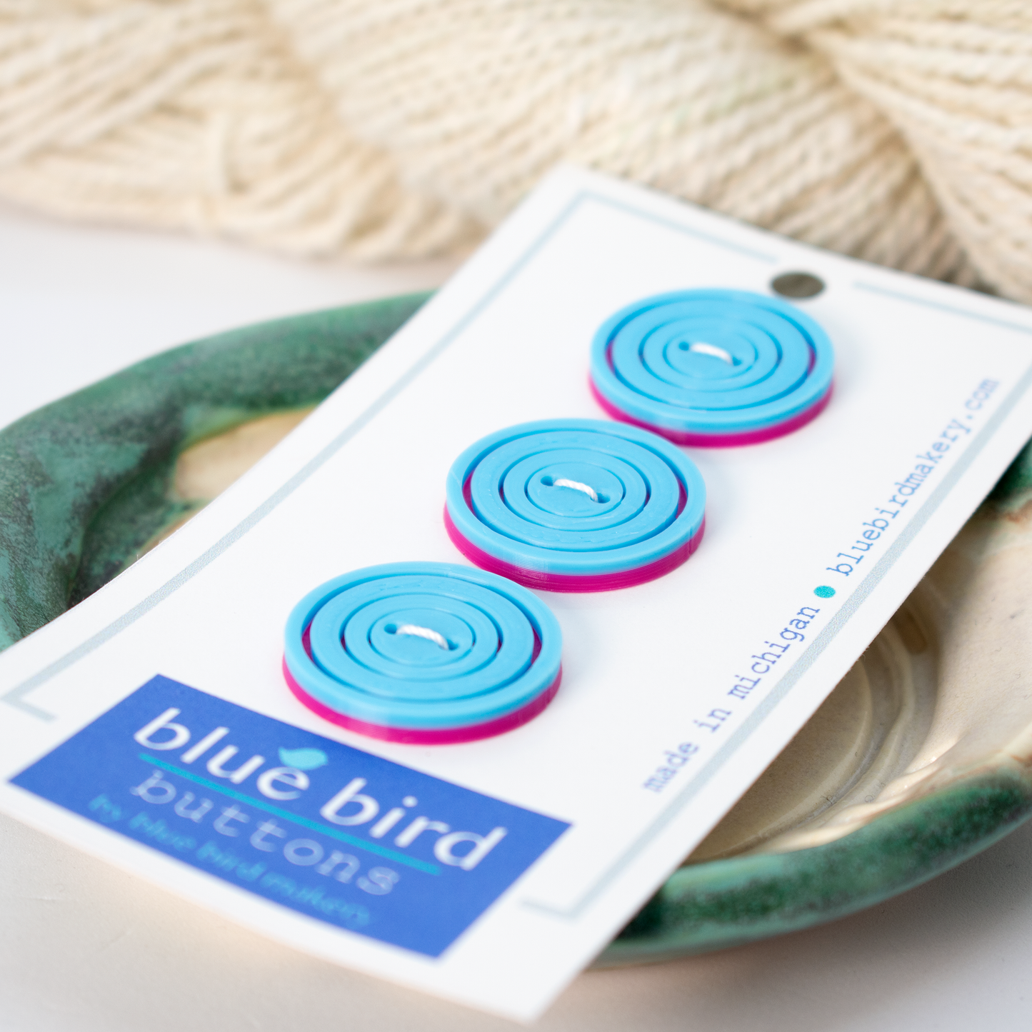 Blue Bird Makery buttons in pastel blue and pink colors on a card for crafting projects