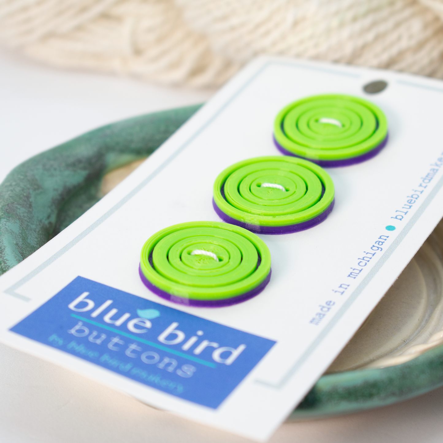 Colorful green and purple blue bird makery buttons displayed on a card for crafting projects