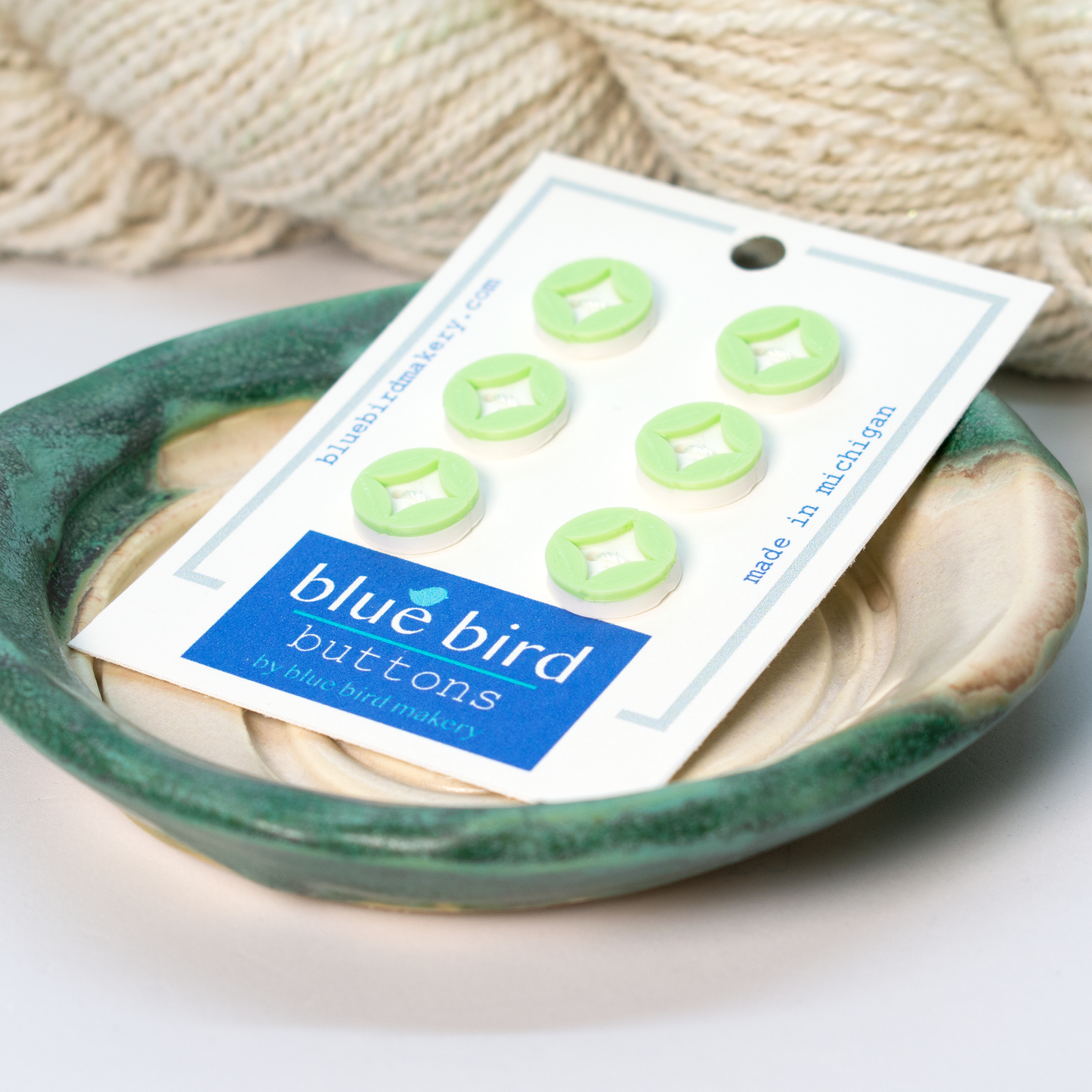 Blue Bird Makery craft supplies featuring green diamond buttons displayed on a ceramic dish