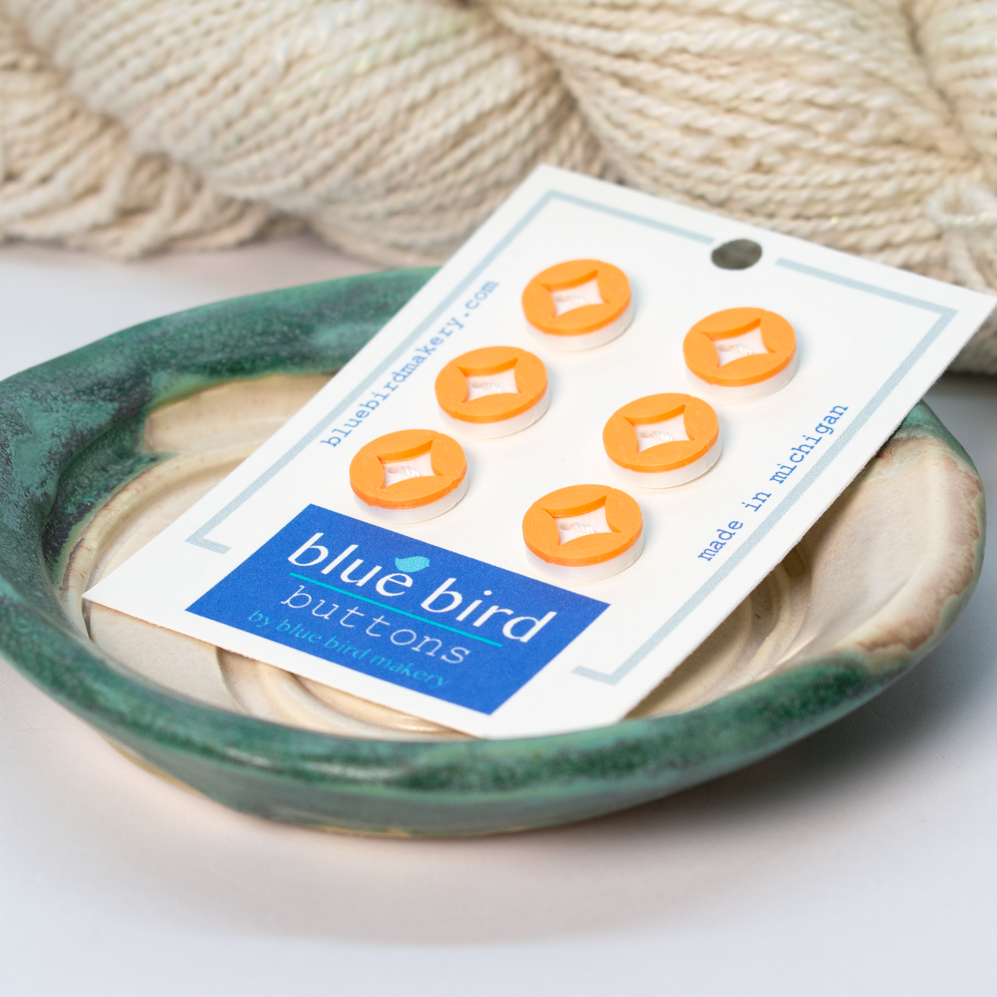 Blue Bird Makery craft supplies featuring orange buttons arranged on a decorative bowl