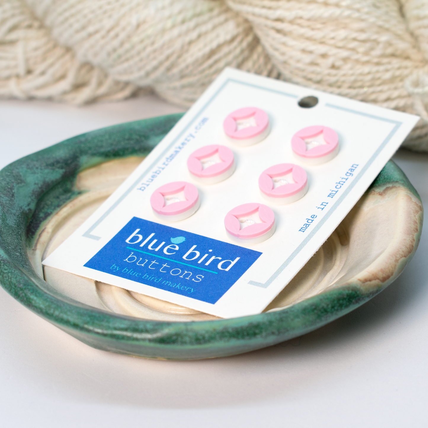 Blue Bird Makery craft supplies featuring pink buttons on a display card in a ceramic dish