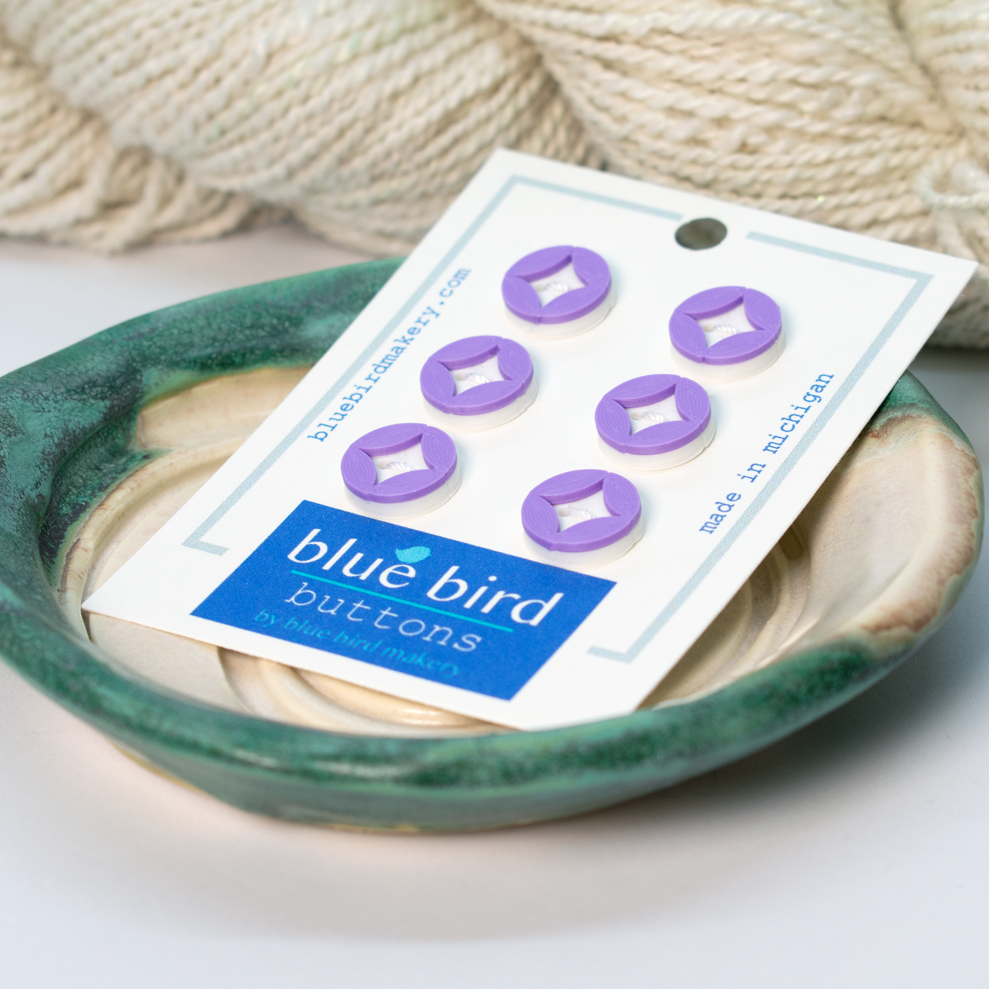 Blue Bird Makery craft supplies, featuring six purple buttons displayed on a ceramic dish