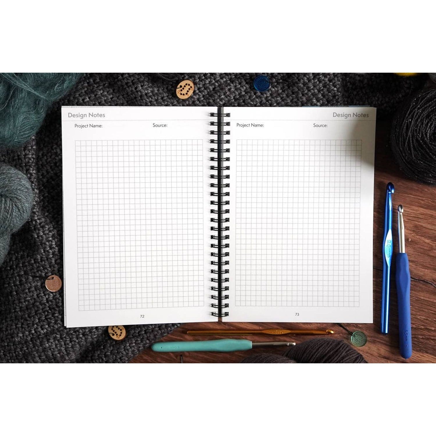 Open spiral crochet pattern organizer notebook with grid design pages surrounded by yarn hooks and buttons