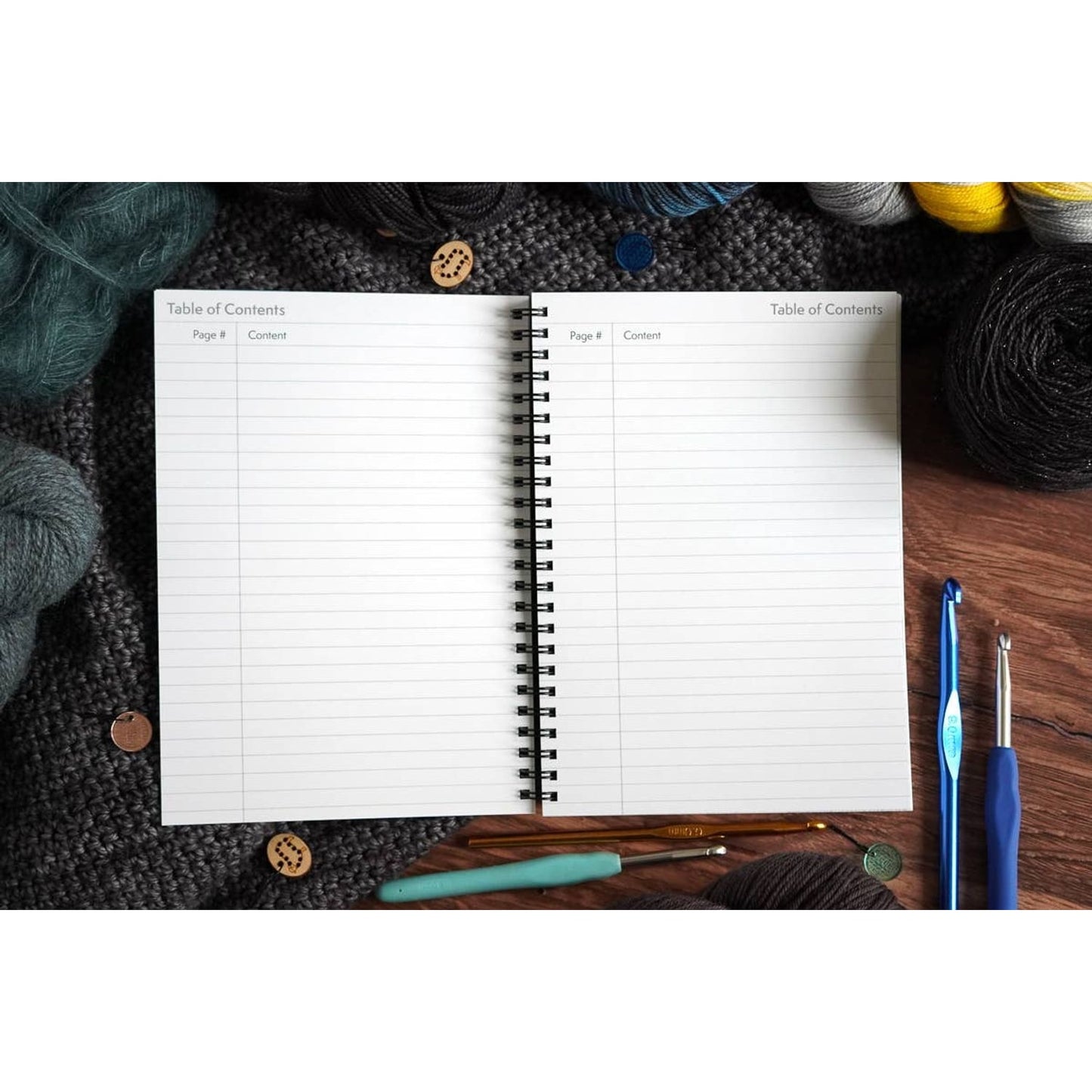 Open spiral crochet pattern organizer notebook with table of contents pages surrounded by yarn and hooks