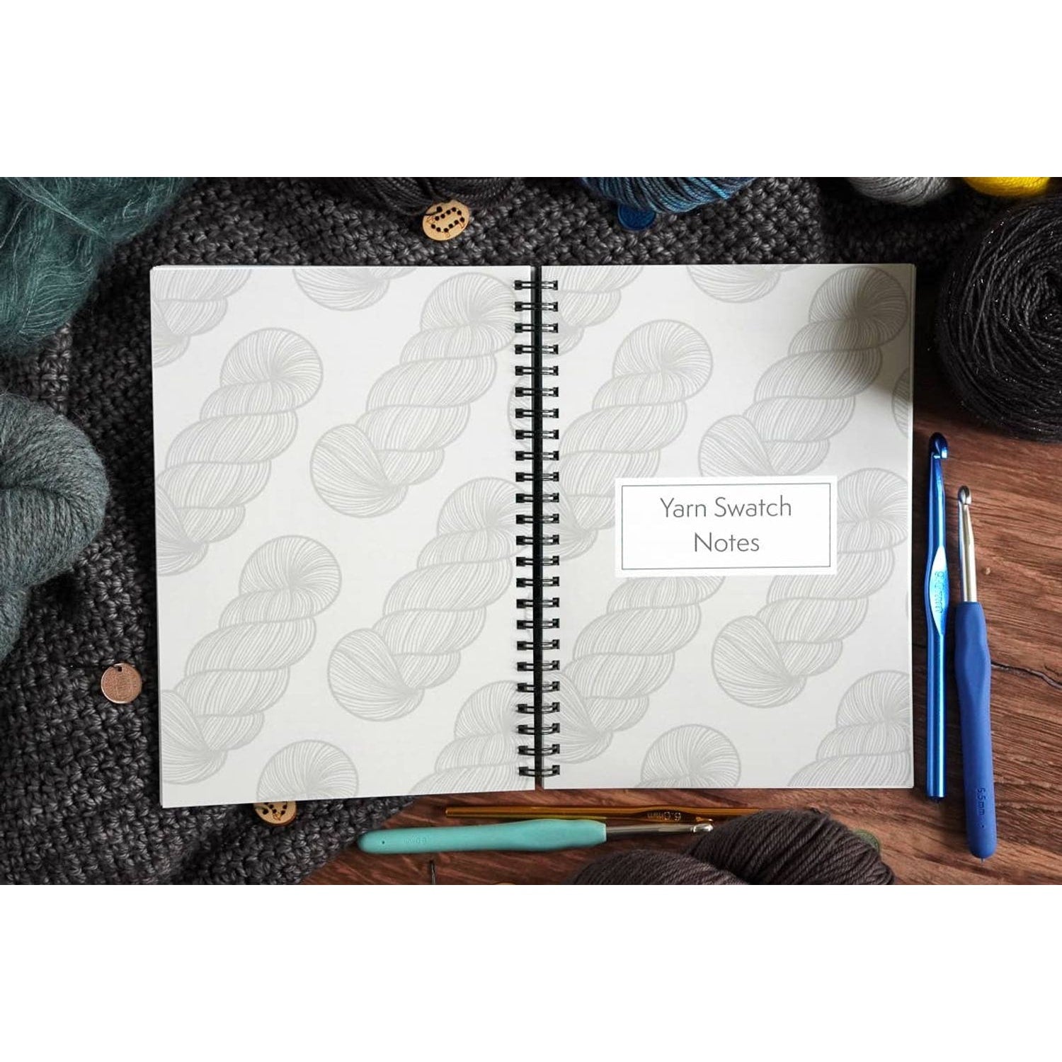 crochet pattern organizer notebook open to Yarn Swatch Notes page surrounded by yarn skeins crochet hooks and wooden buttons