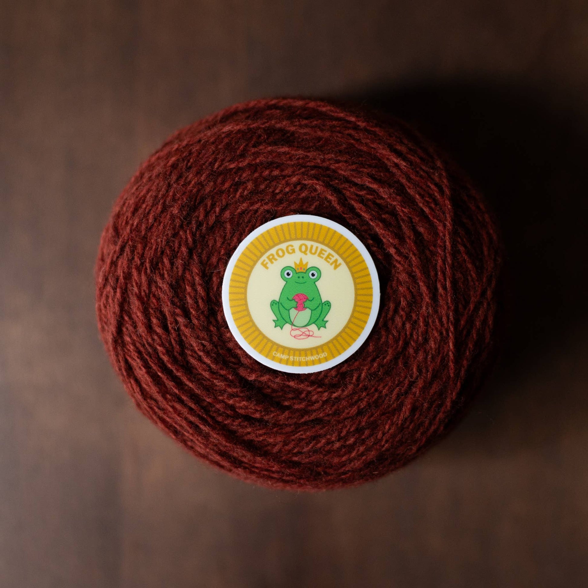 Brown yarn ball labeled Frog Queen with a colorful name badge sticker on top