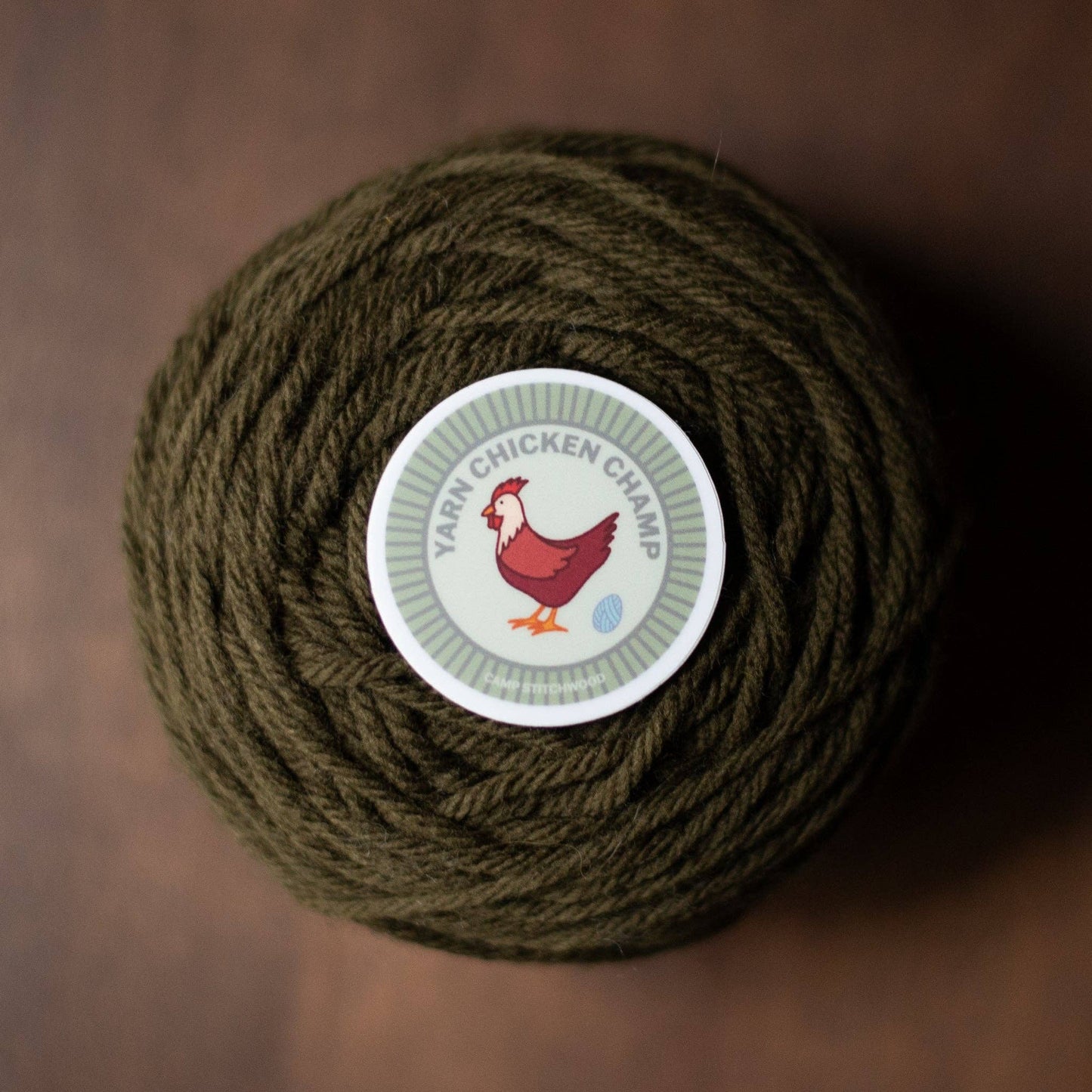 Camp Stitchwood Yarn Chicken Champ Ball of Green Yarn with Name Badge Sticker on Top