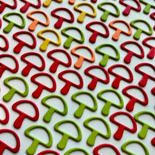 Colorful mushroom shaped sewing notions from Comma Craft Co arranged in rows on white background