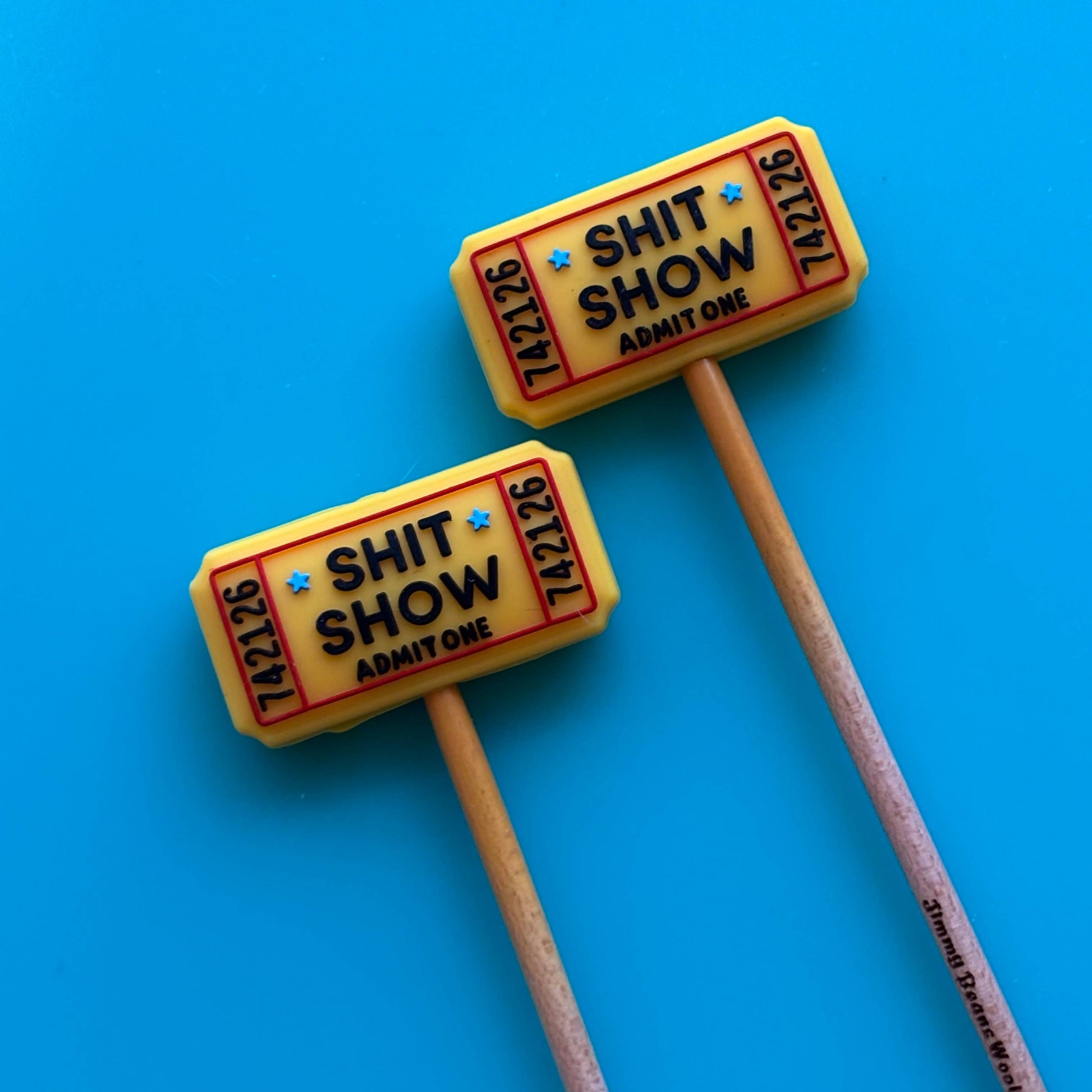 Two yellow ticket shaped Comma Craft Co needle protectors. Wooden needles reading SHIT SHOW on blue background