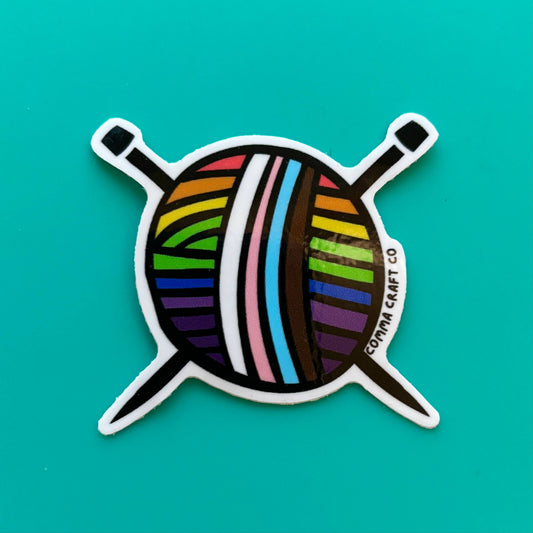 Comma Craft Co intersectional pride knitting sticker featuring colorful yarn ball with knitting needles