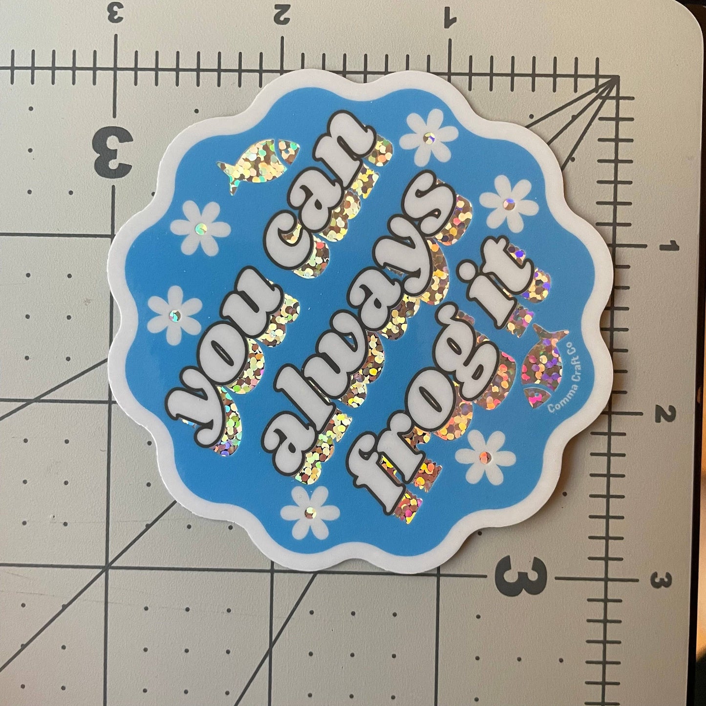 Blue scalloped sticker with holographic letters and daisies reading knitting sticker you can always frog it.