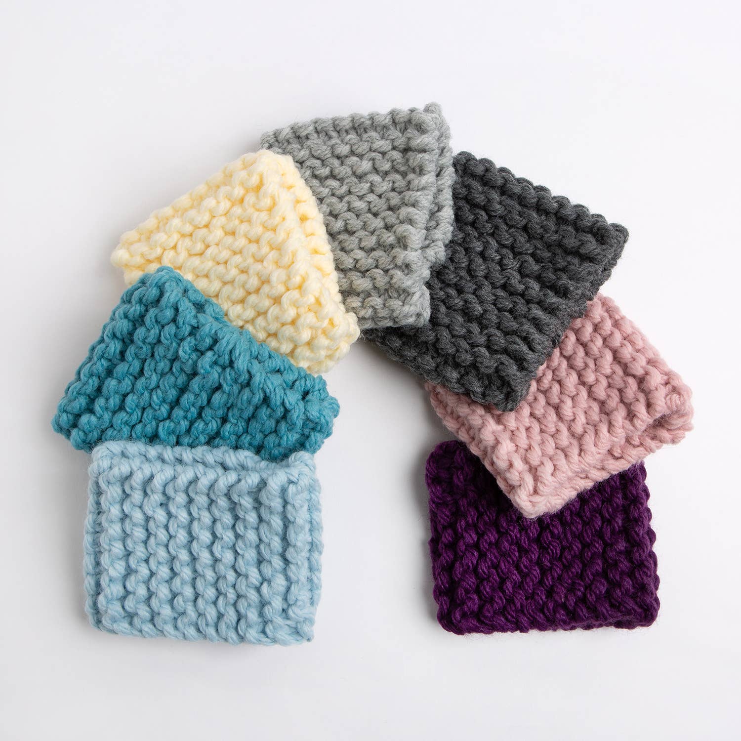 Wool Couture Company beginner knitting kit for cup cozy with seven chunky knit cup cozies in pastel and jewel tones