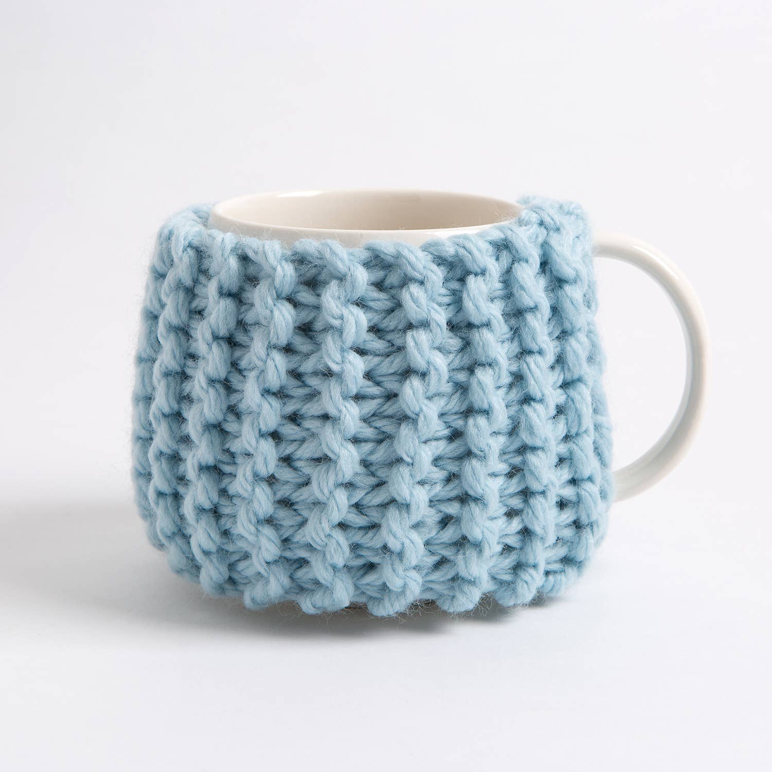 Light blue chunky knit mug cozy on white ceramic cup beginner knitting kit for cup cozy by Wool Couture Company
