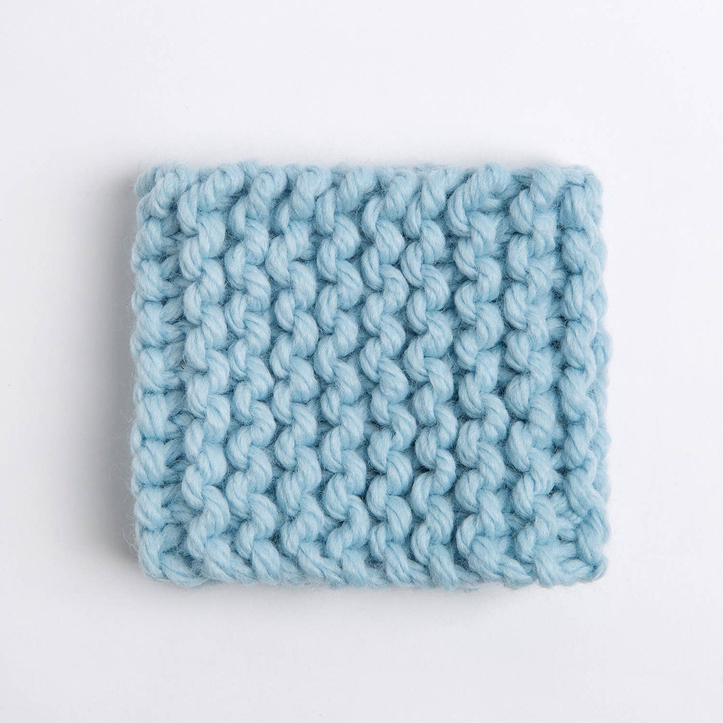 Light blue chunky hand knitted cup cozy square on white background beginner knitting kit for cup cozy