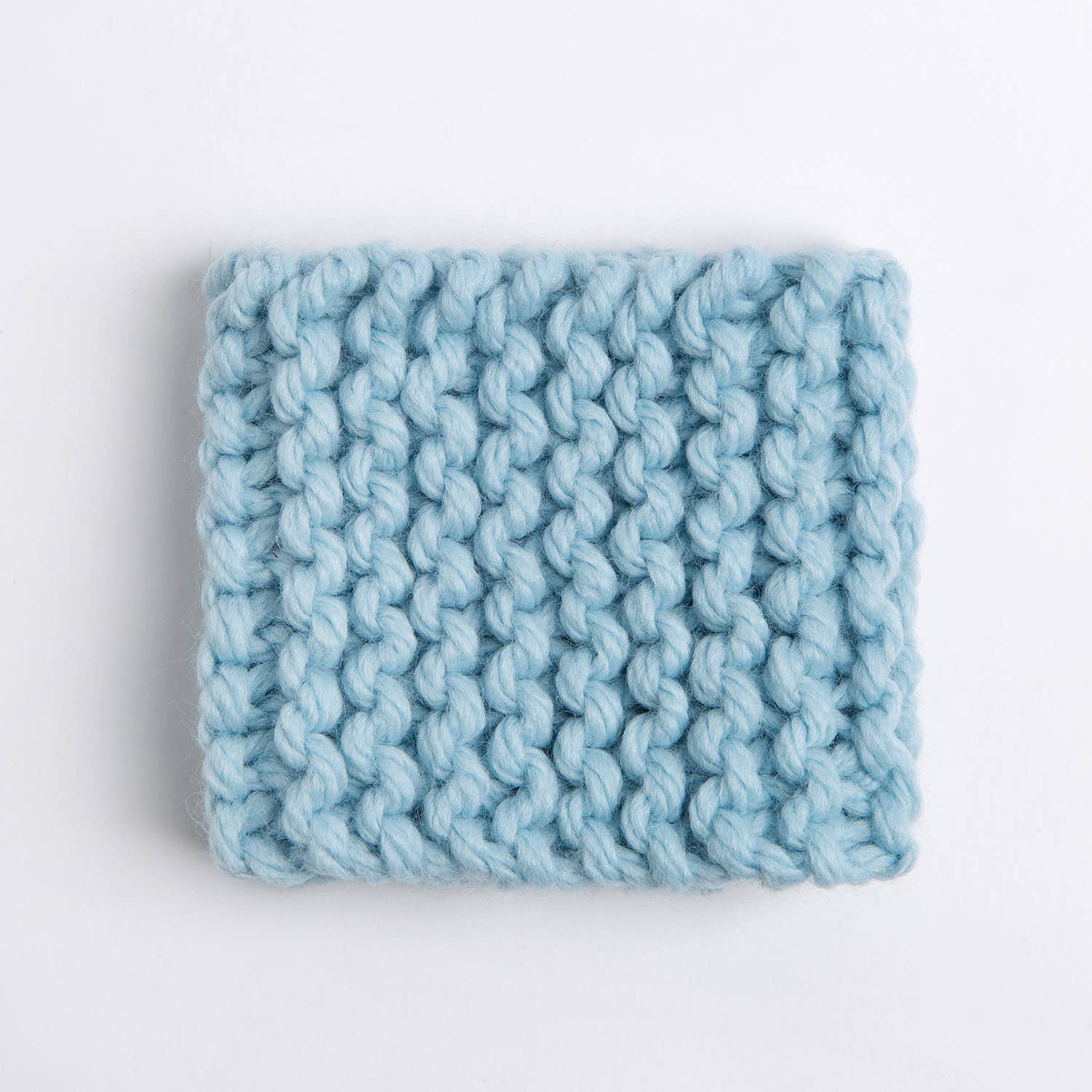 Light blue chunky hand knitted cup cozy square on white background beginner knitting kit for cup cozy