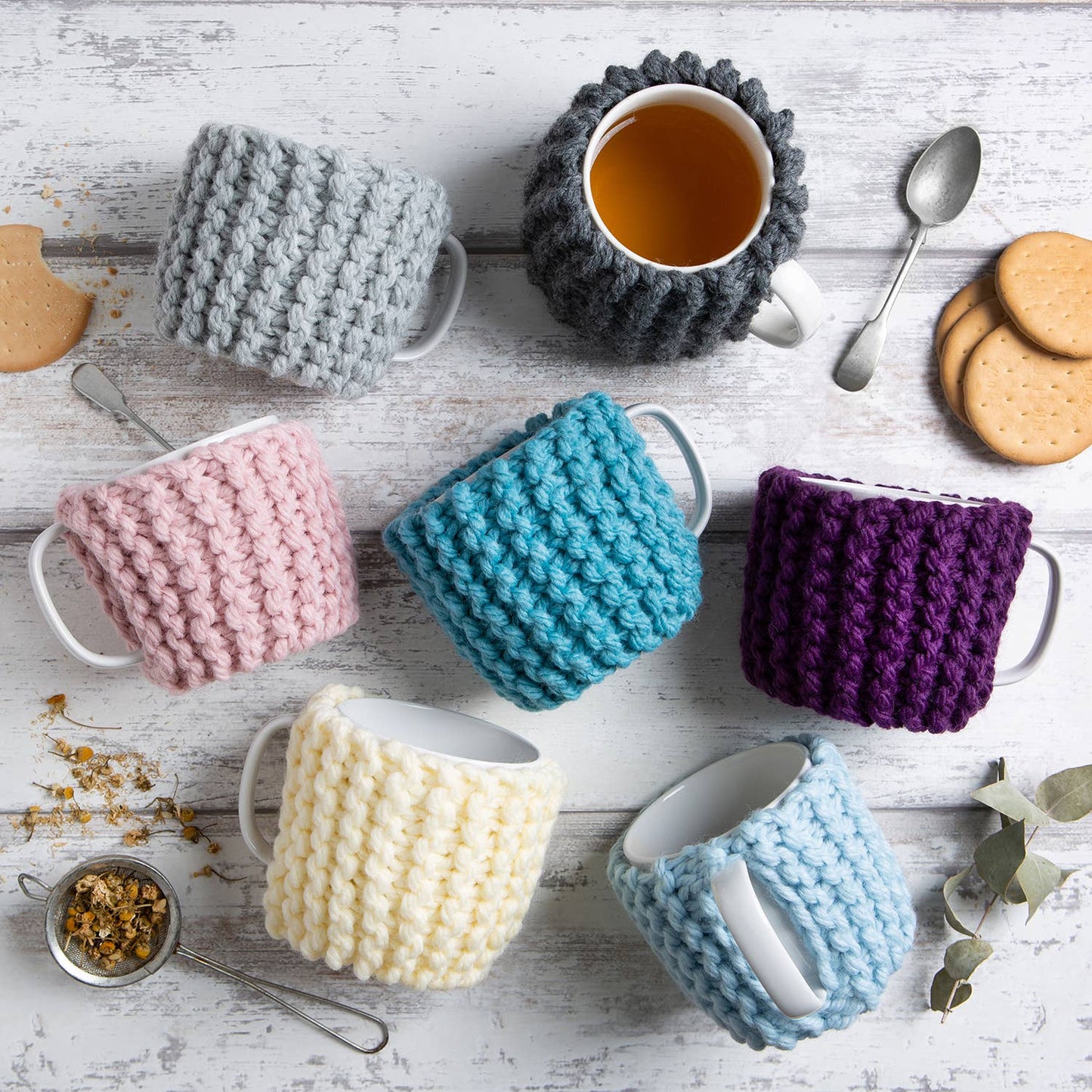 Wool Couture Company colorful knitted mug cozies with tea and cookies showing beginner knitting kit for cup cozy