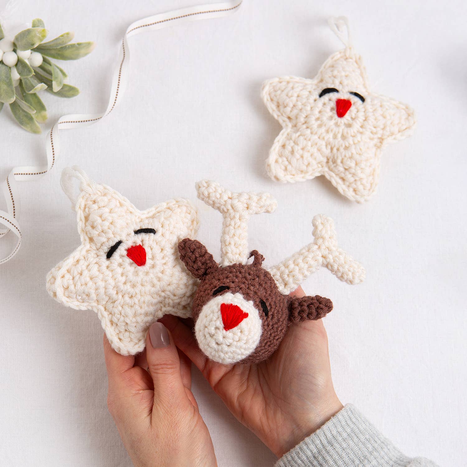 Belle the Reindeer crochet pattern brown reindeer head ornament with red heart nose and two cream star ornaments held in han…
