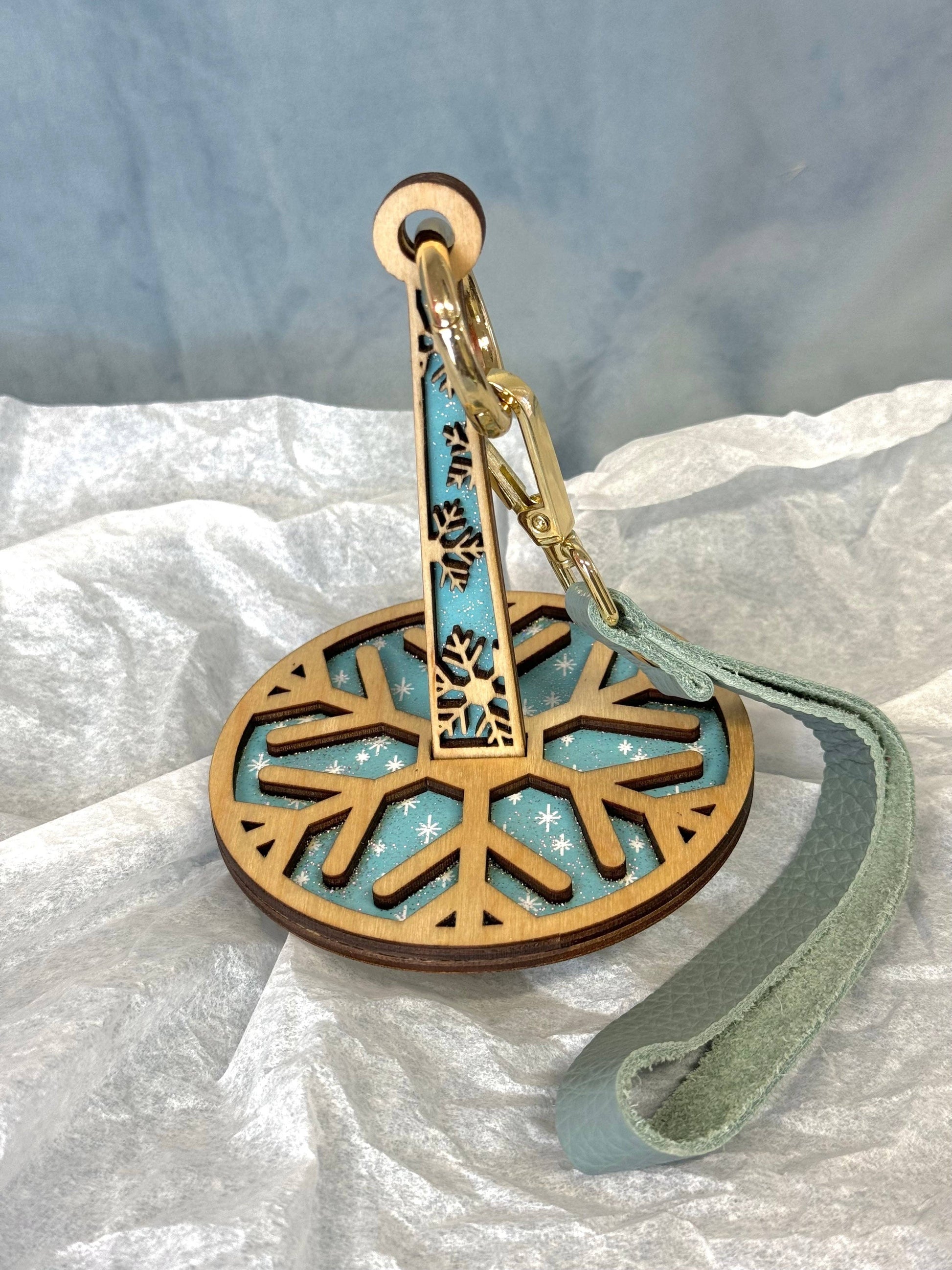 lemonwood snowflake yarn holder wooden snowflake disk with teal backing metal clip and leather wrist strap